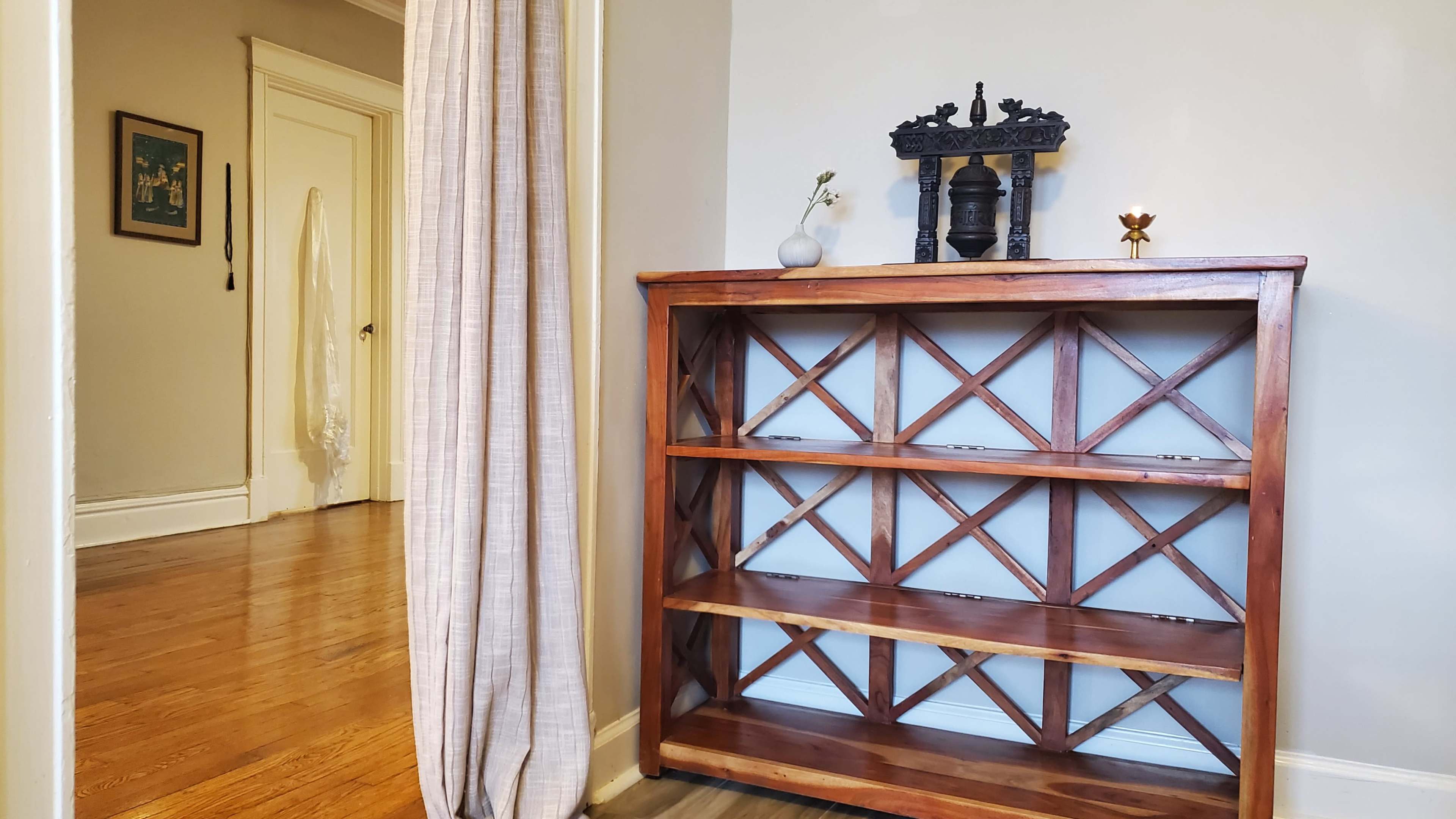 A wooden bookshelf with an open design stands against a wall, beside a draped curtain leading to another room.