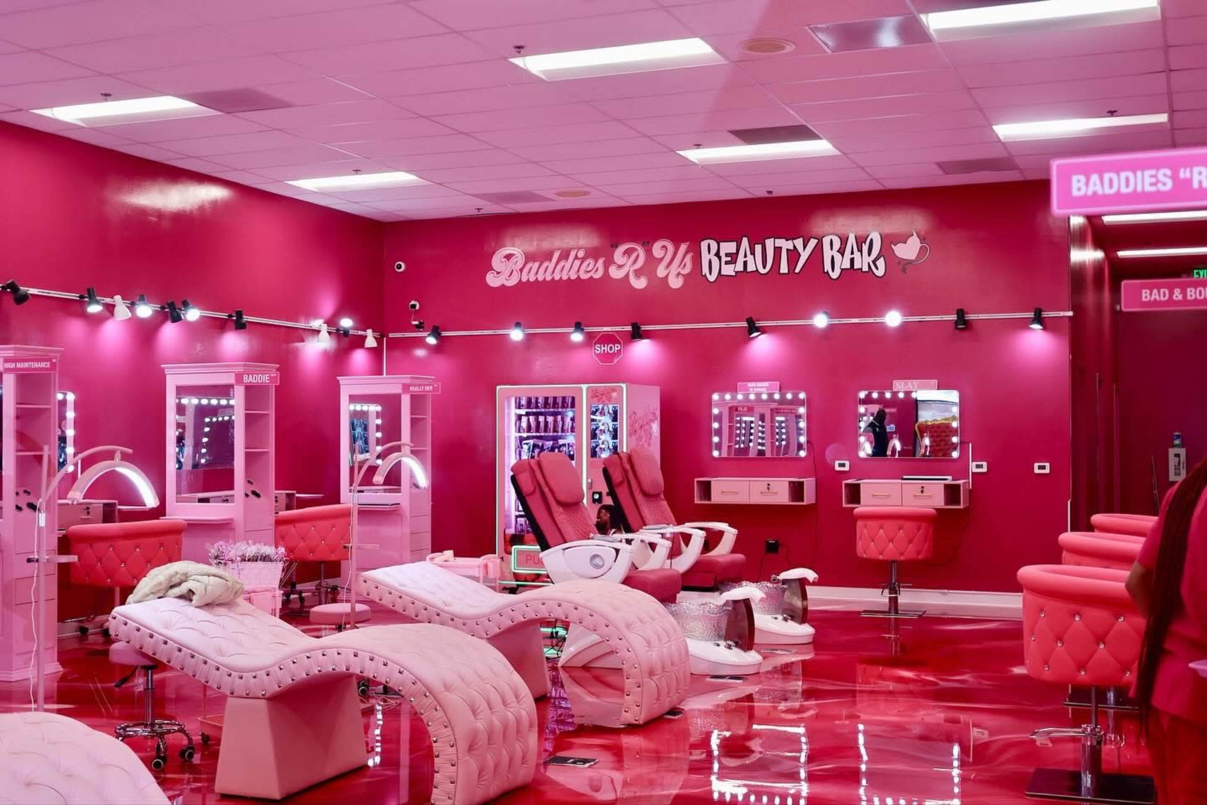 The image shows a brightly lit beauty bar interior with pink decor, featuring treatment chairs, mirrors, and lighting.