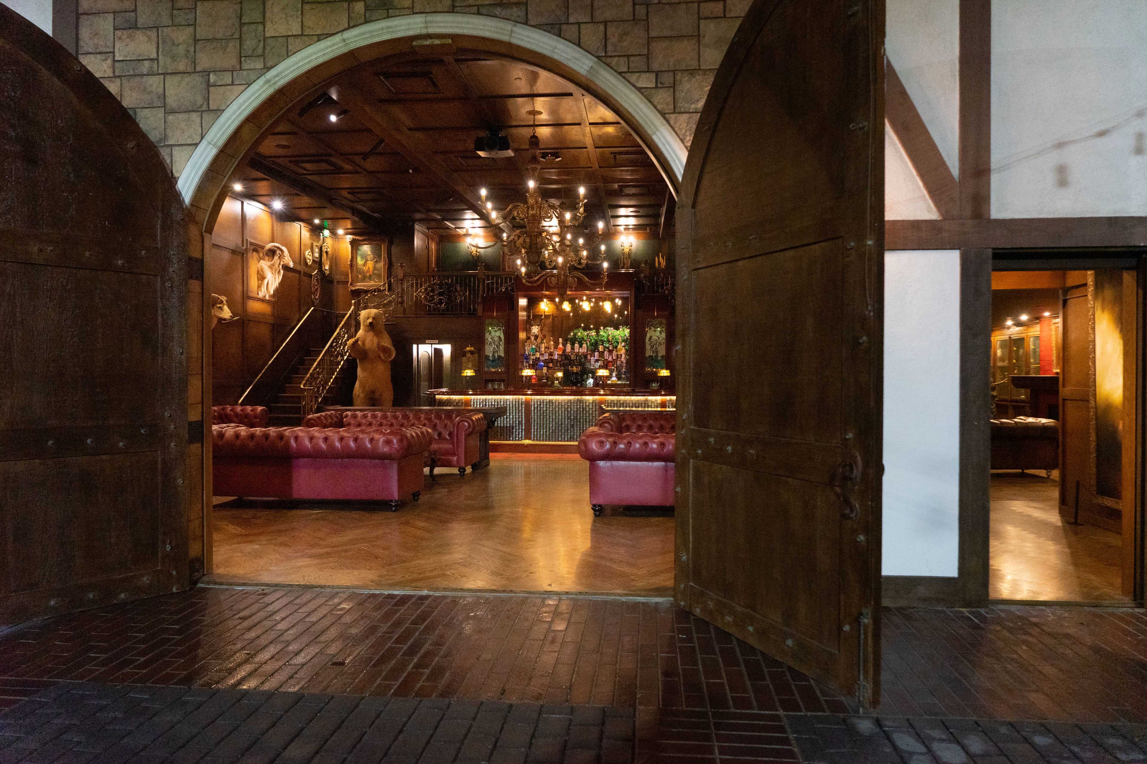 An expansive bar area with red leather couches and a wooden bar, framed by large open double doors.