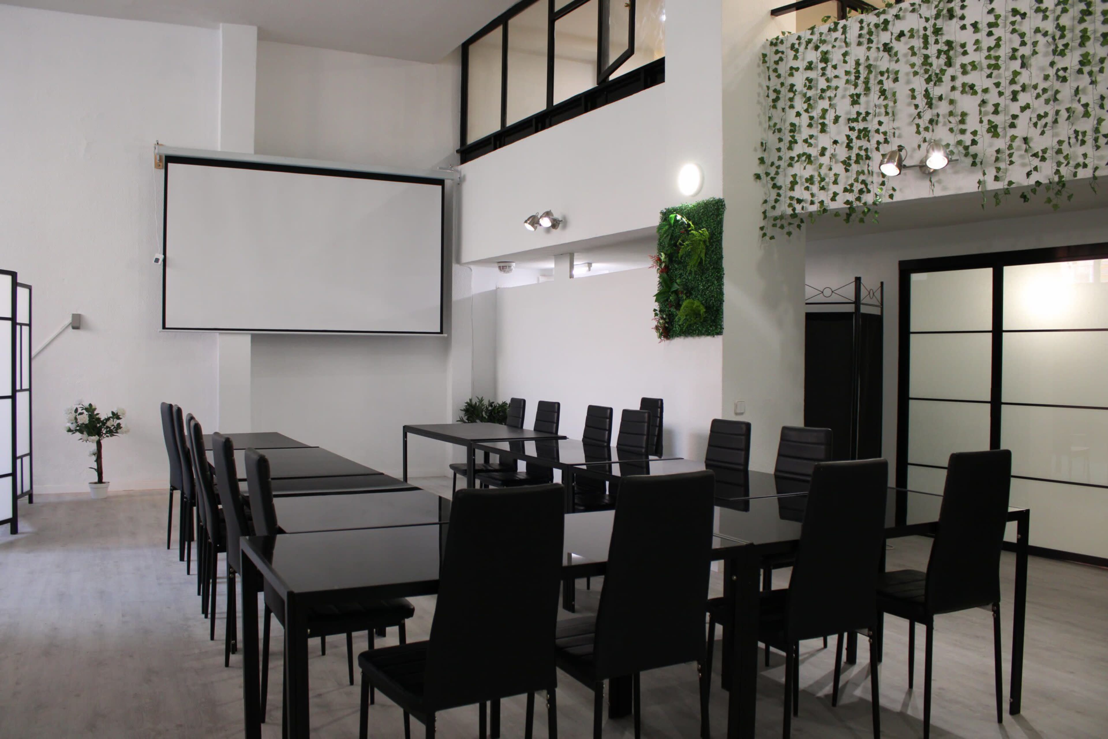 The image shows a modern conference room with a large screen, several black chairs, and a greenery wall decoration.