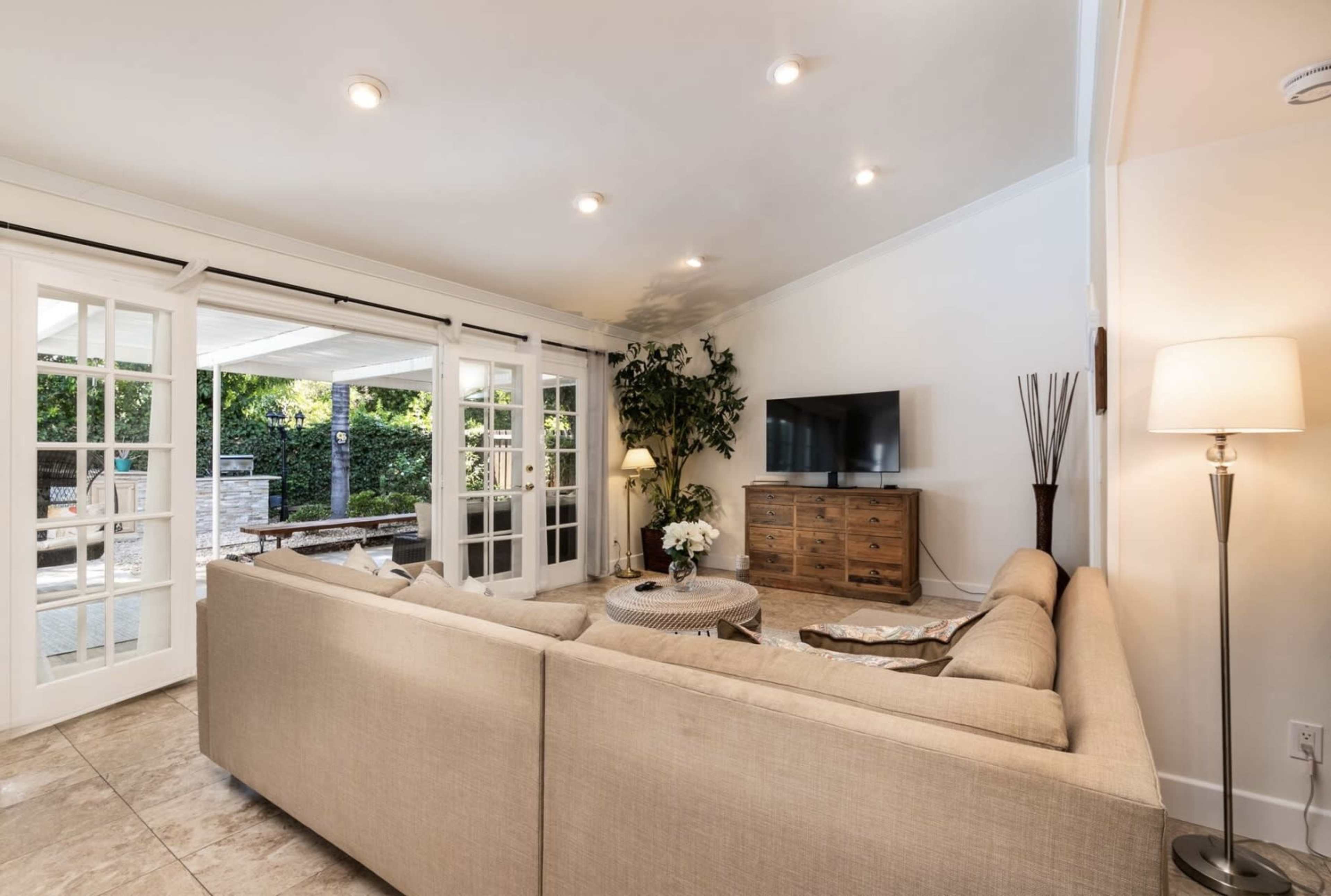 A modern living room features a sectional sofa, a wooden TV cabinet, and large glass doors leading to an outdoor area.