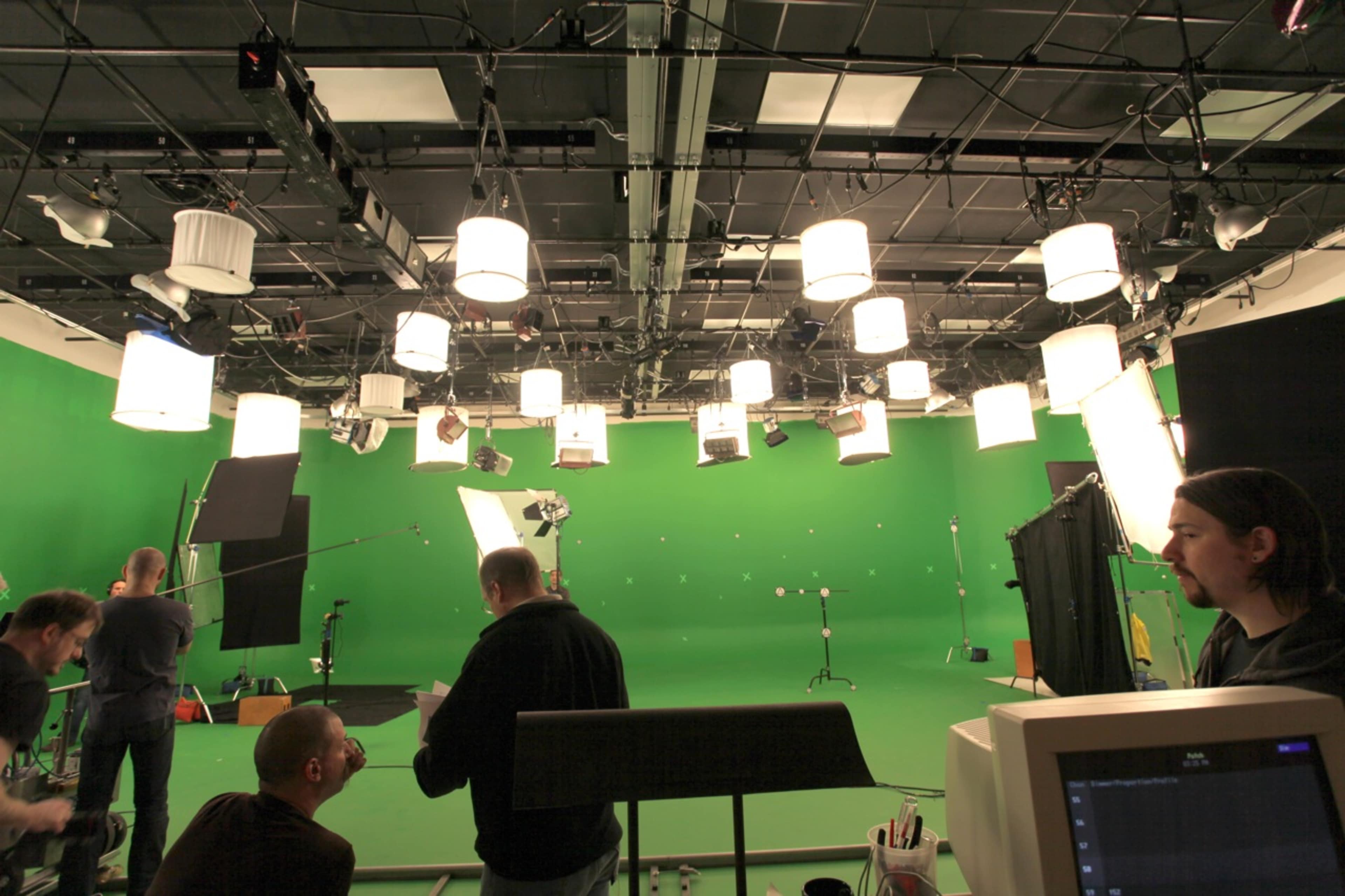 A green screen studio setup with crew members preparing for a shoot, surrounded by various lighting equipment.
