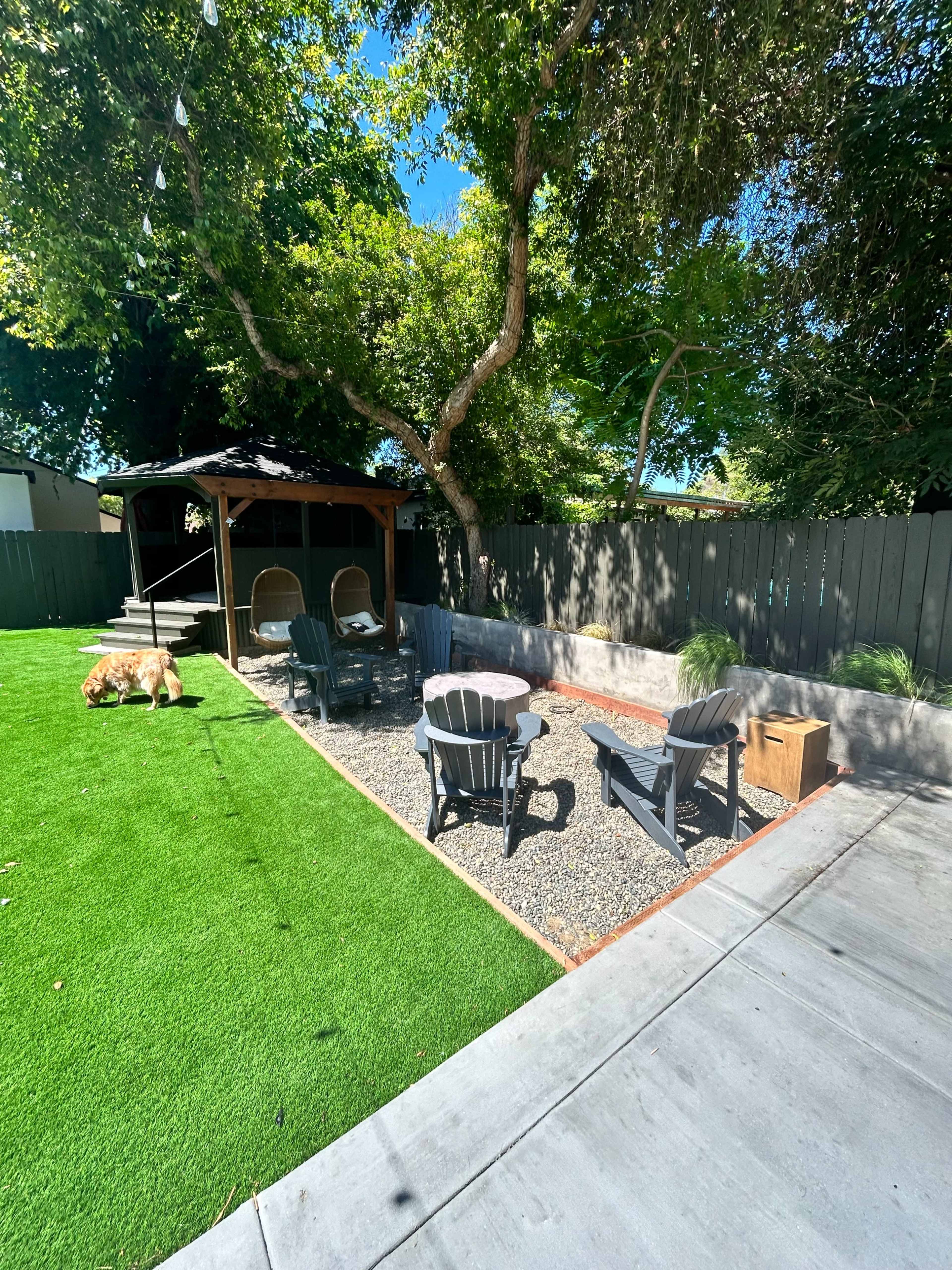 The image features a backyard with a circular gravel seating area surrounded by black chairs and a fire pit, a gazebo in the background, and a green lawn.