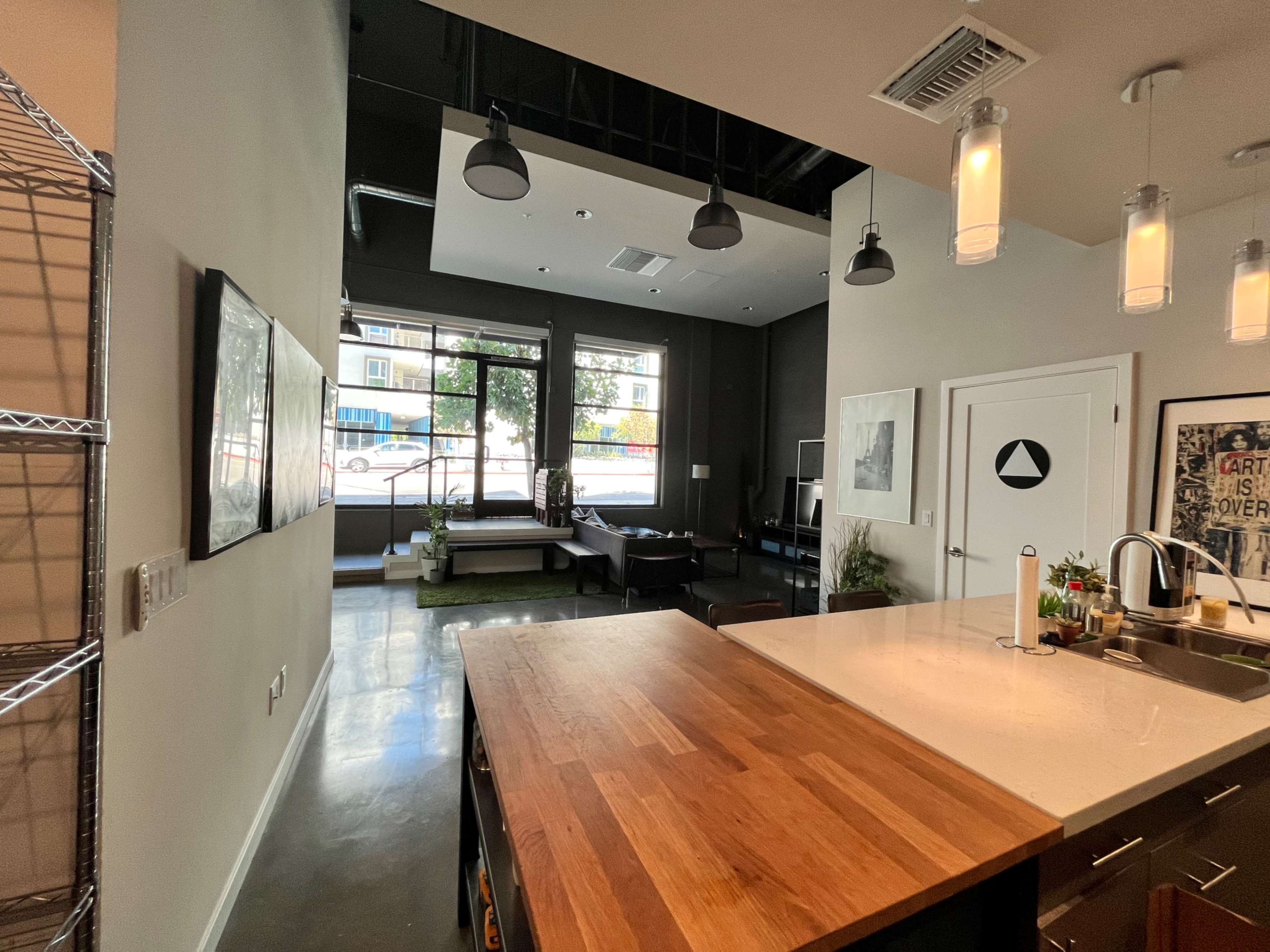 An open-concept apartment kitchen with a wooden island and a view into a spacious living area featuring large windows.