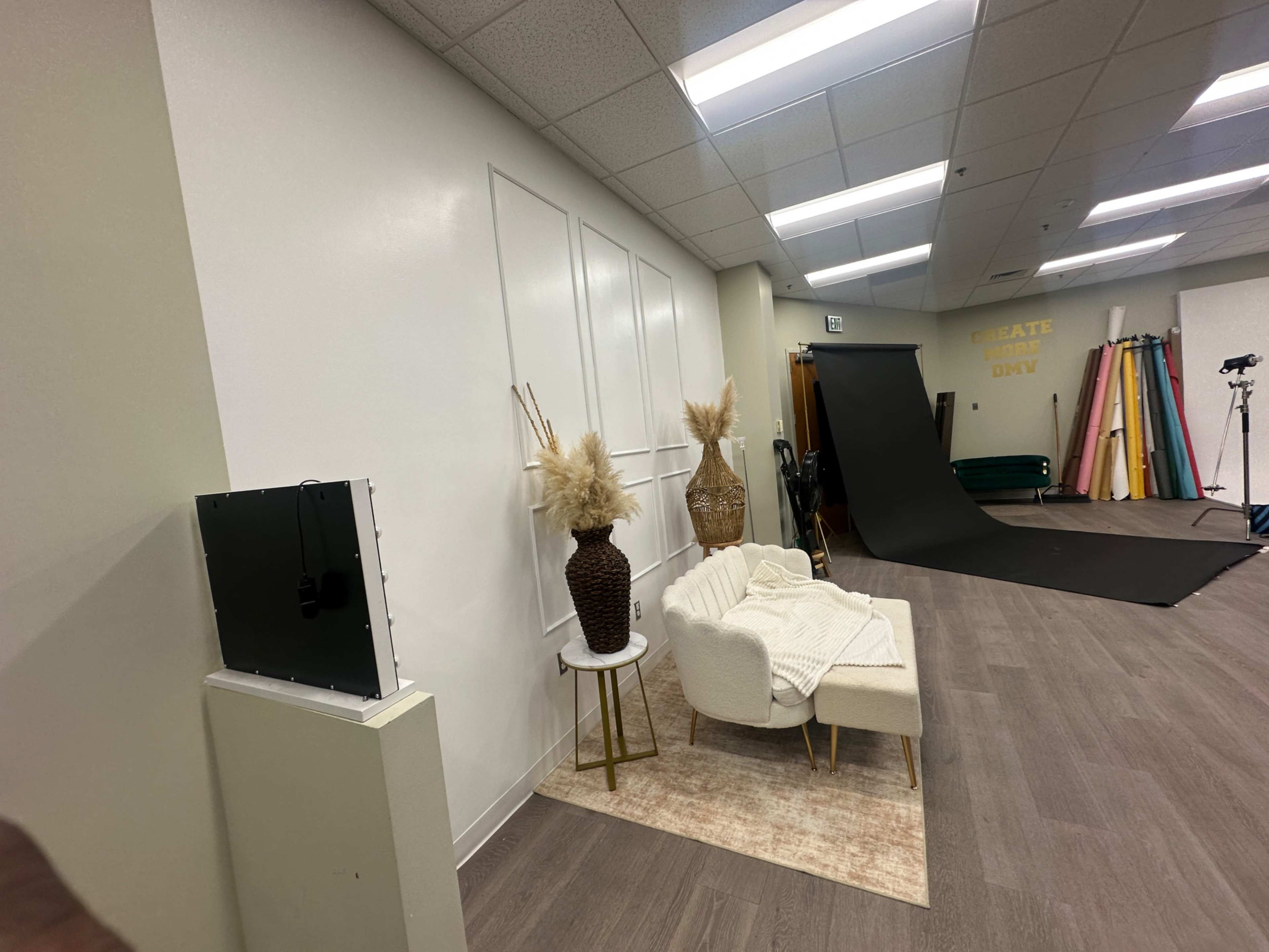 The image shows a studio space with a white wall, a small seating area with a couch and decorative vases, and various backdrops arranged in the background.