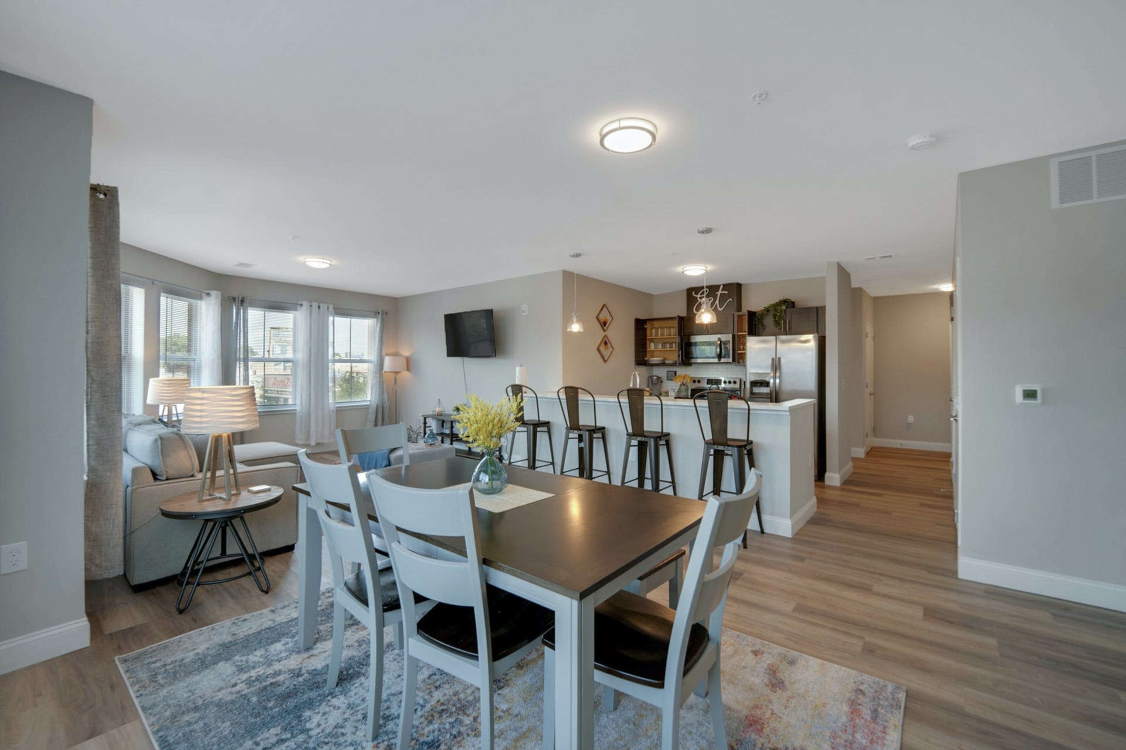 A modern open-concept living and dining area with a table, chairs, and a kitchen in the background.