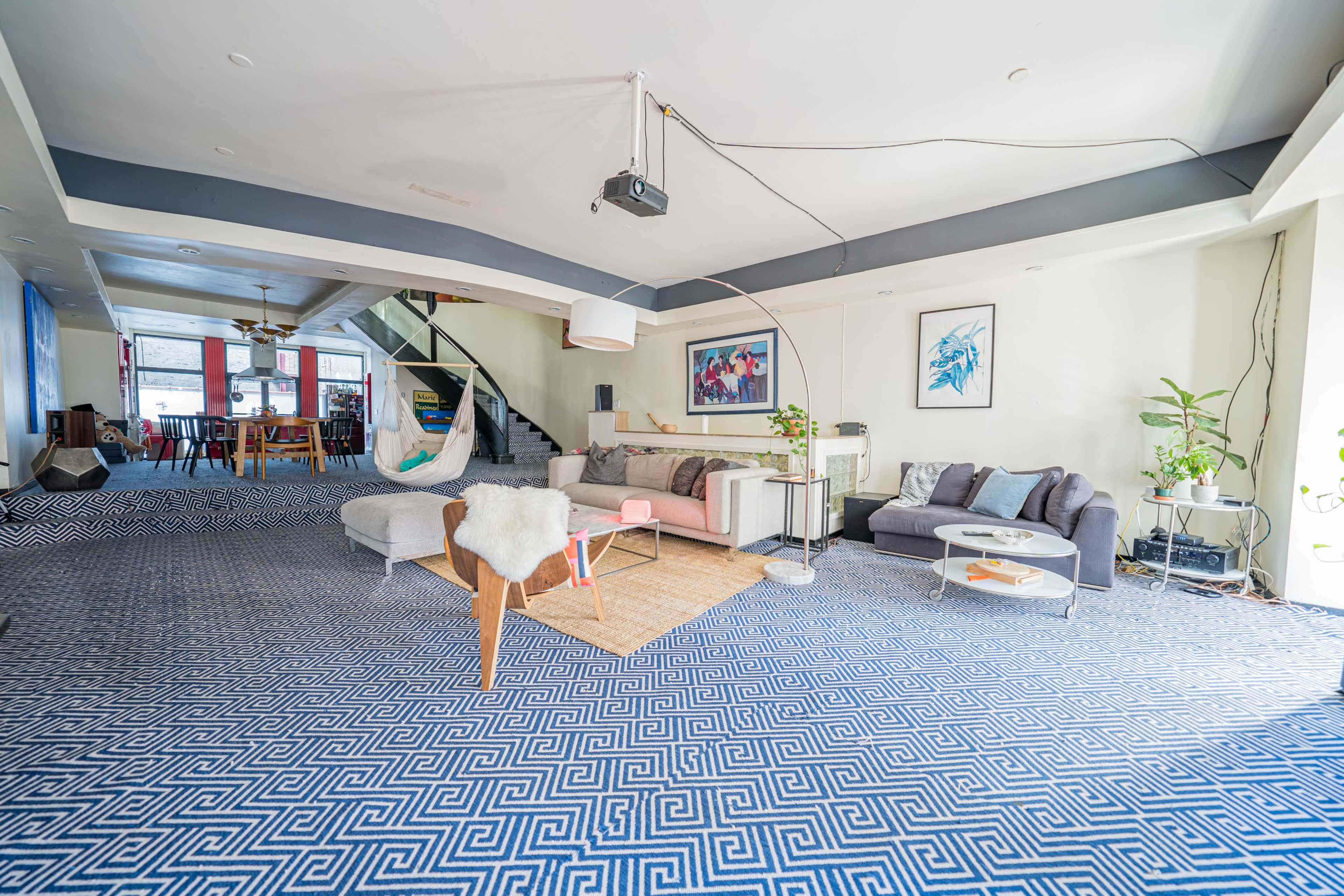 A spacious room with a patterned blue carpet, modern furniture, and an open layout that includes a staircase and various seating areas.