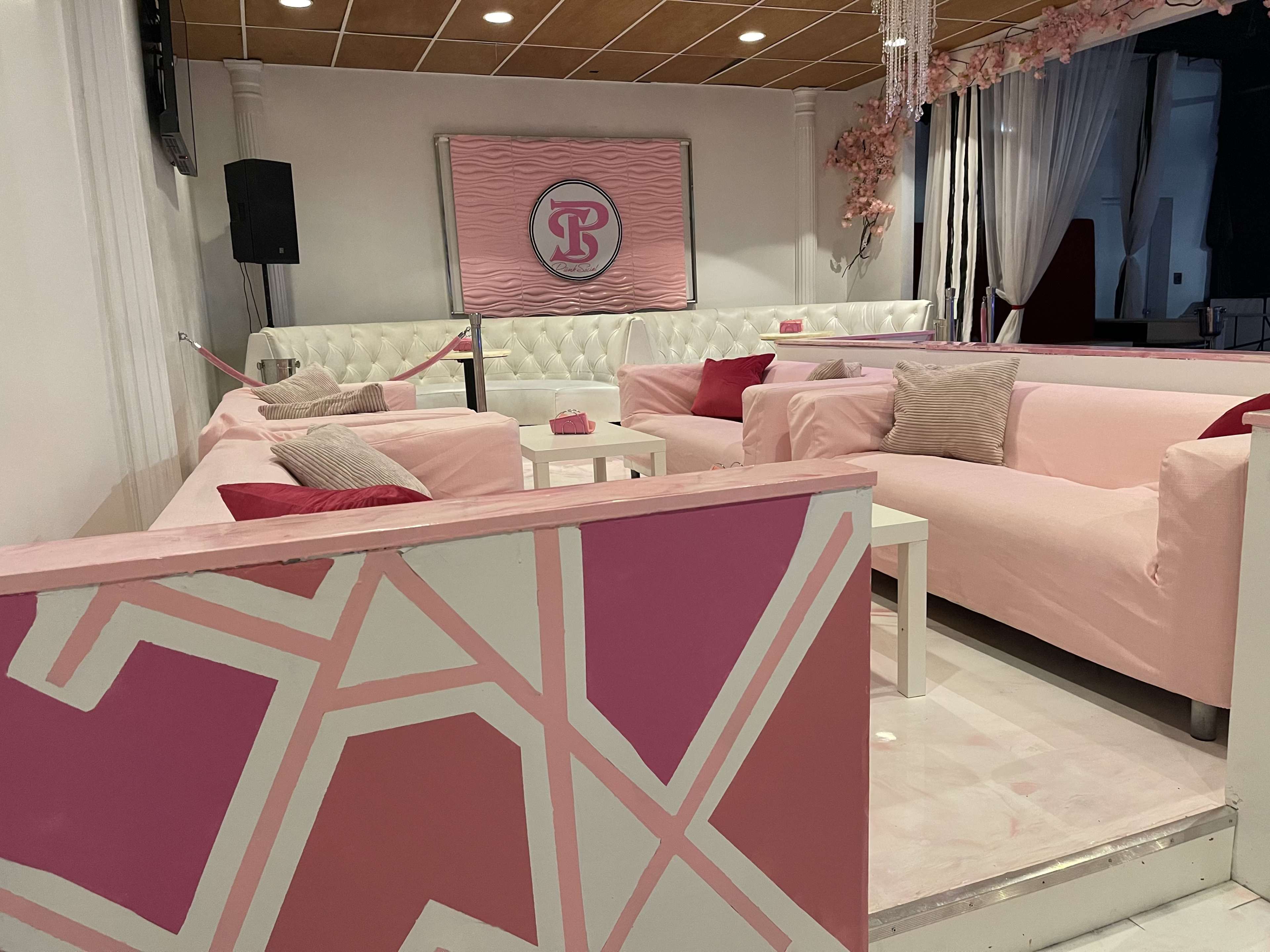 The image shows a modern lounge area with pink upholstered furniture, white walls, and decorative accents featuring geometric patterns.