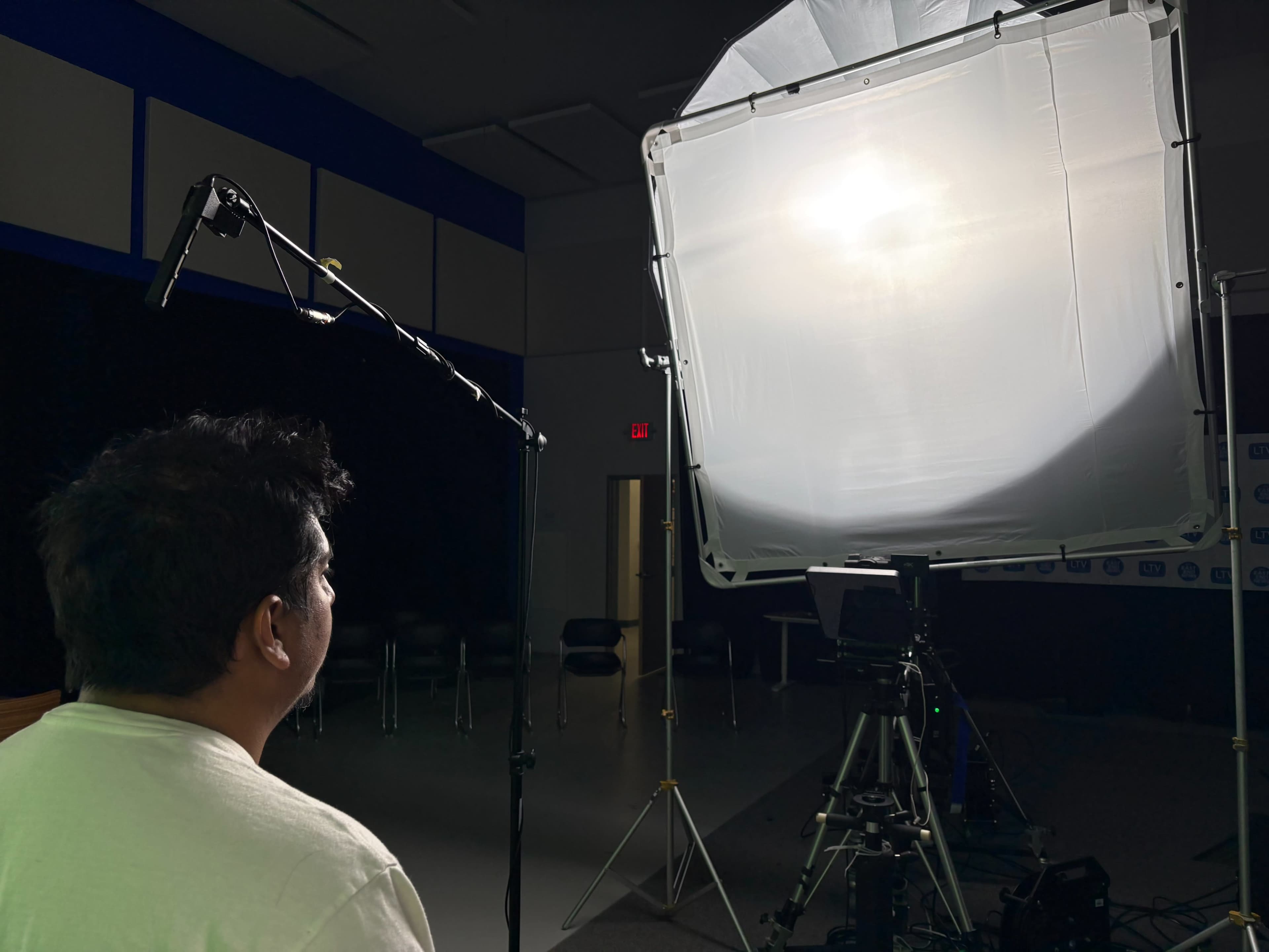 A person stands in front of a bright light source mounted on a stand in a studio setting.