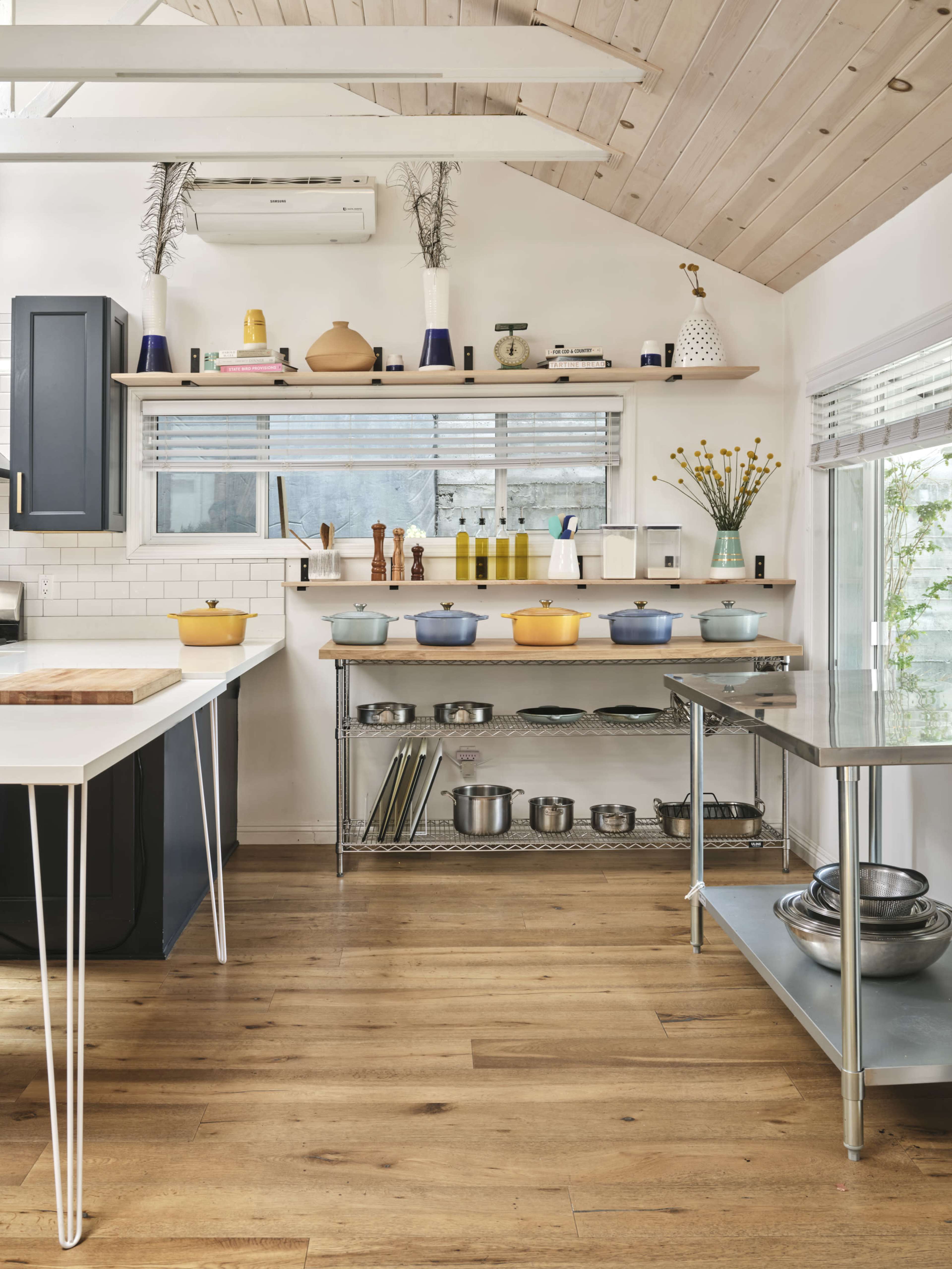 A modern kitchen features wooden flooring, open shelving with cookware, and a large island with a butcher block countertop.