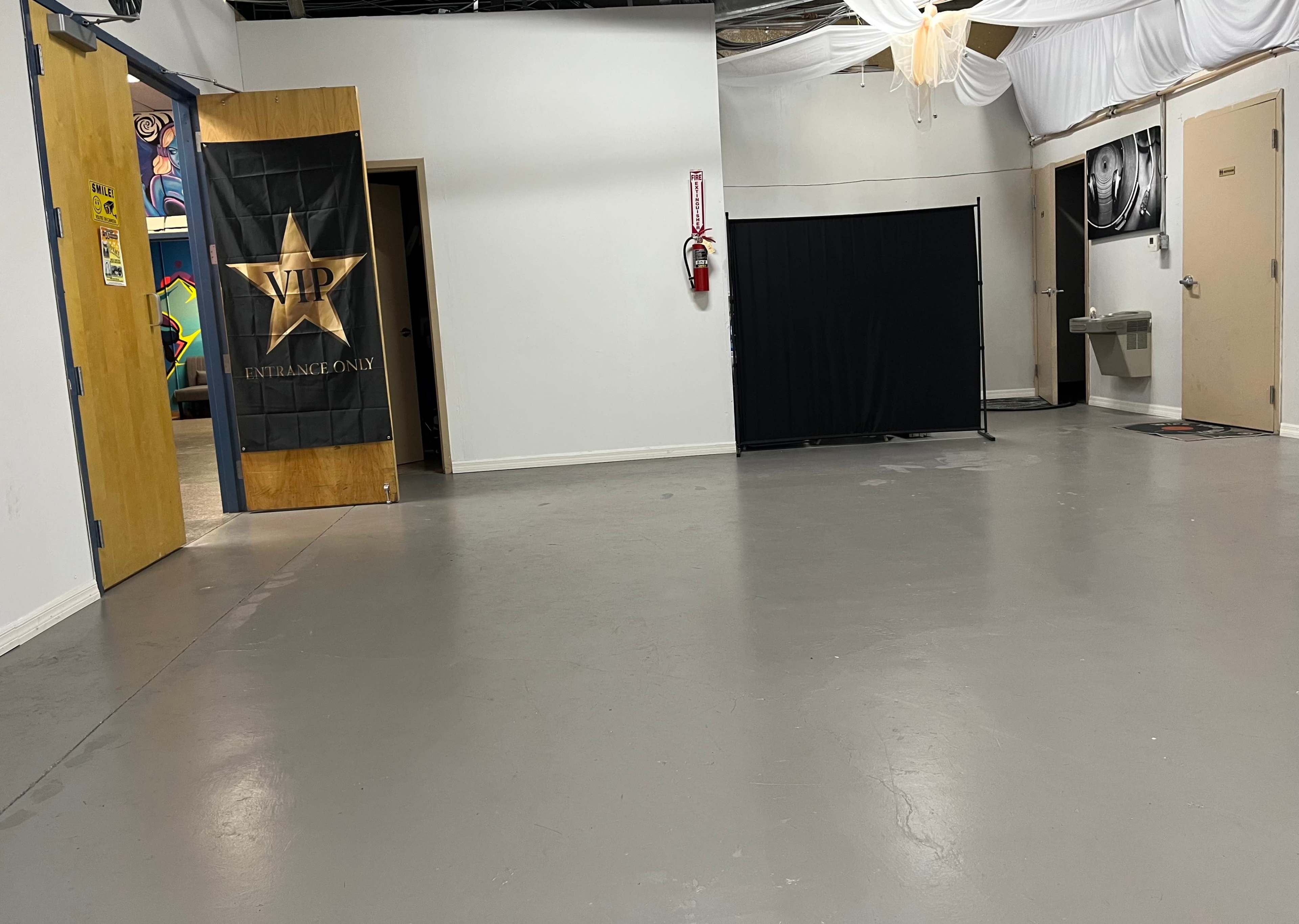 The image shows a spacious interior room with a VIP entrance banner, multiple doors, a fire extinguisher, and a water fountain.