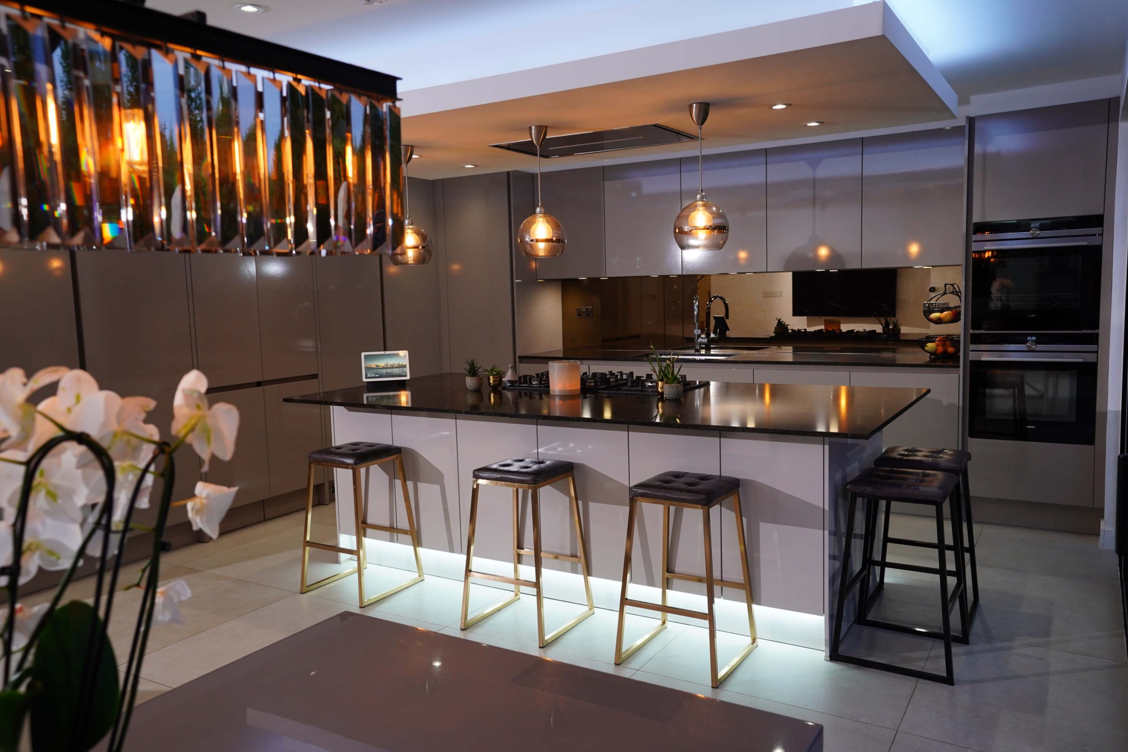 A modern kitchen features a large island with four bar stools, pendant lighting, and sleek cabinets.