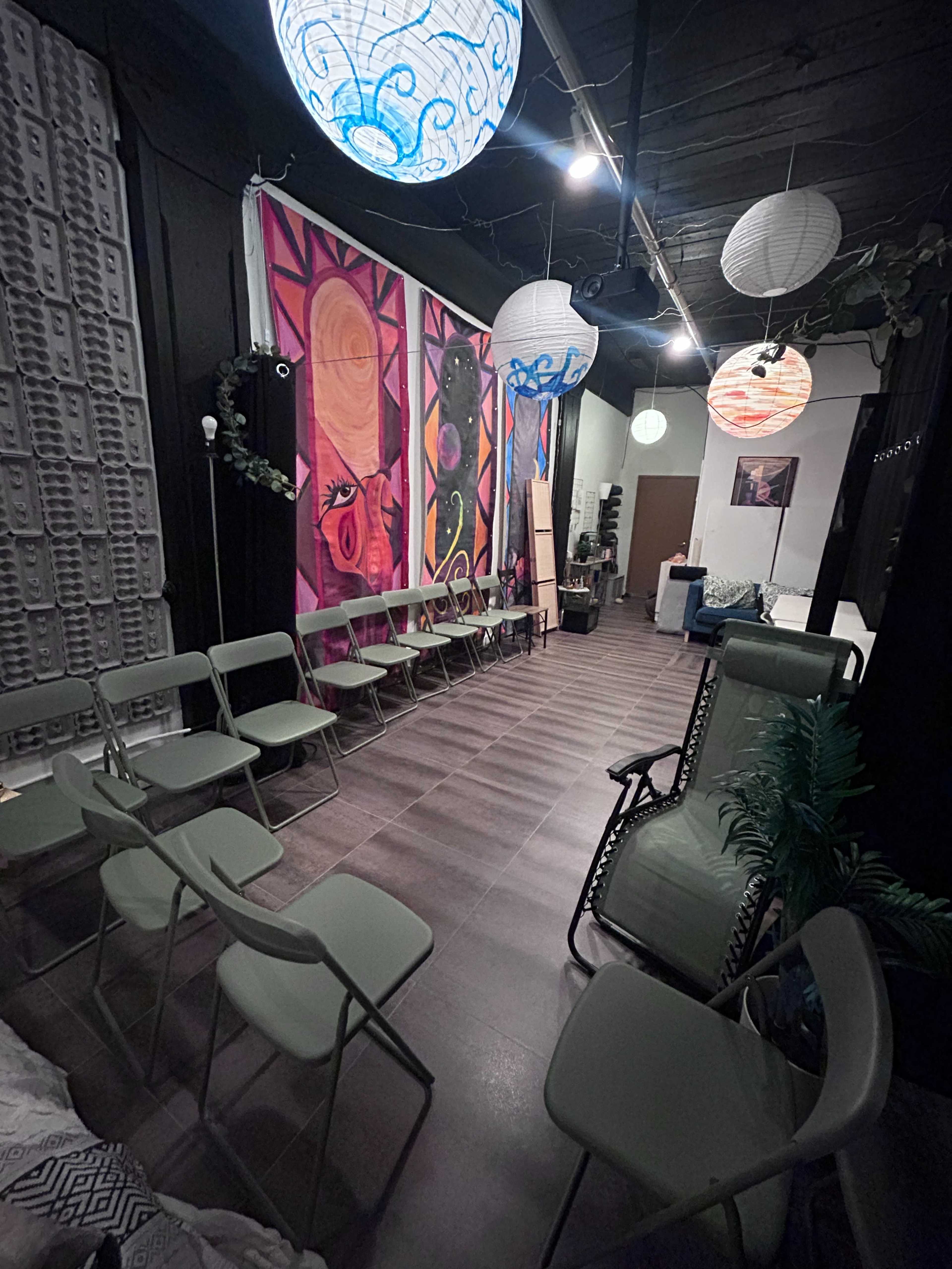 The image shows a room with several chairs arranged in a semi-circle facing colorful murals and hanging paper lanterns.