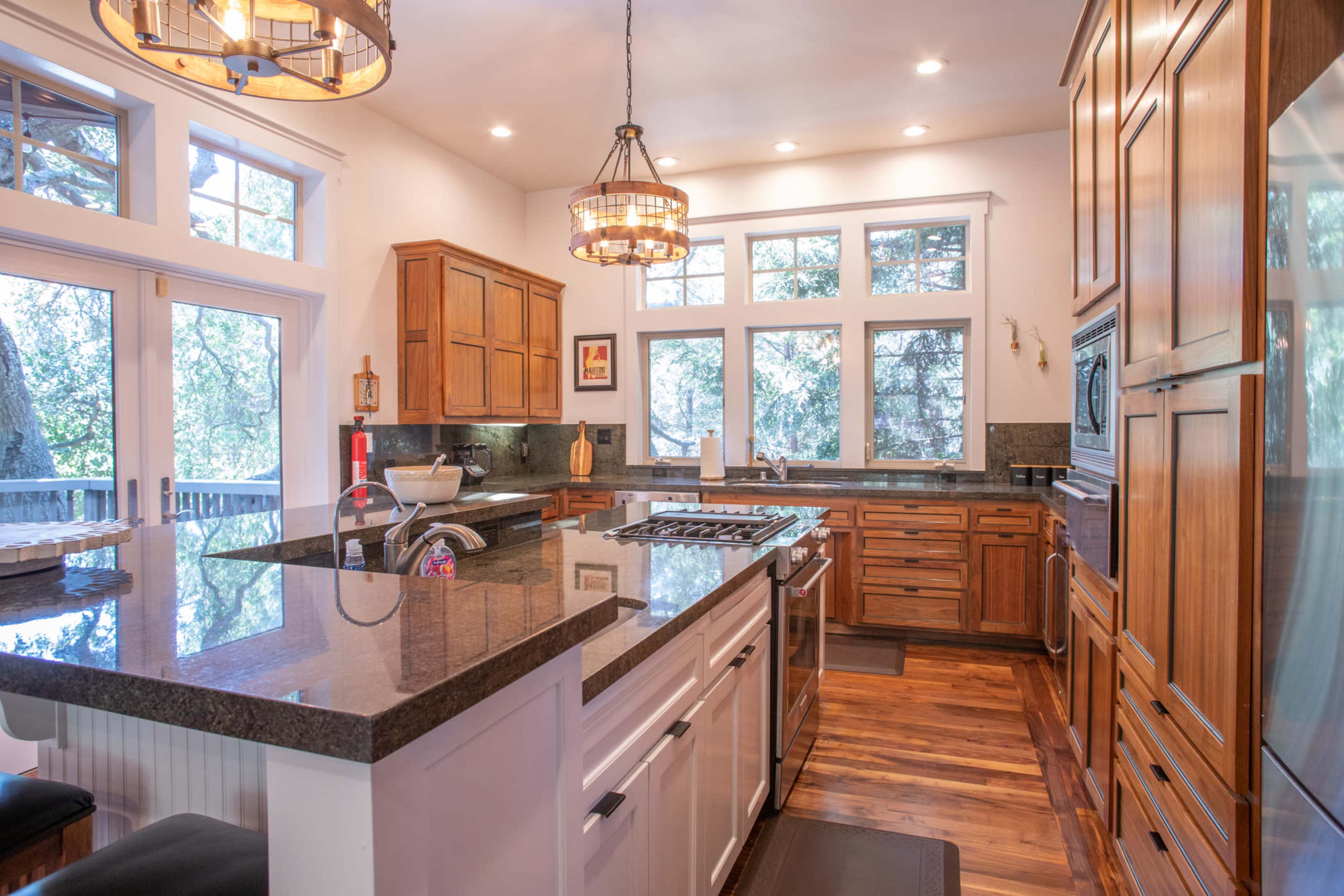 The kitchen features wooden cabinetry, a large island with a dark countertop, and multiple windows providing natural light.