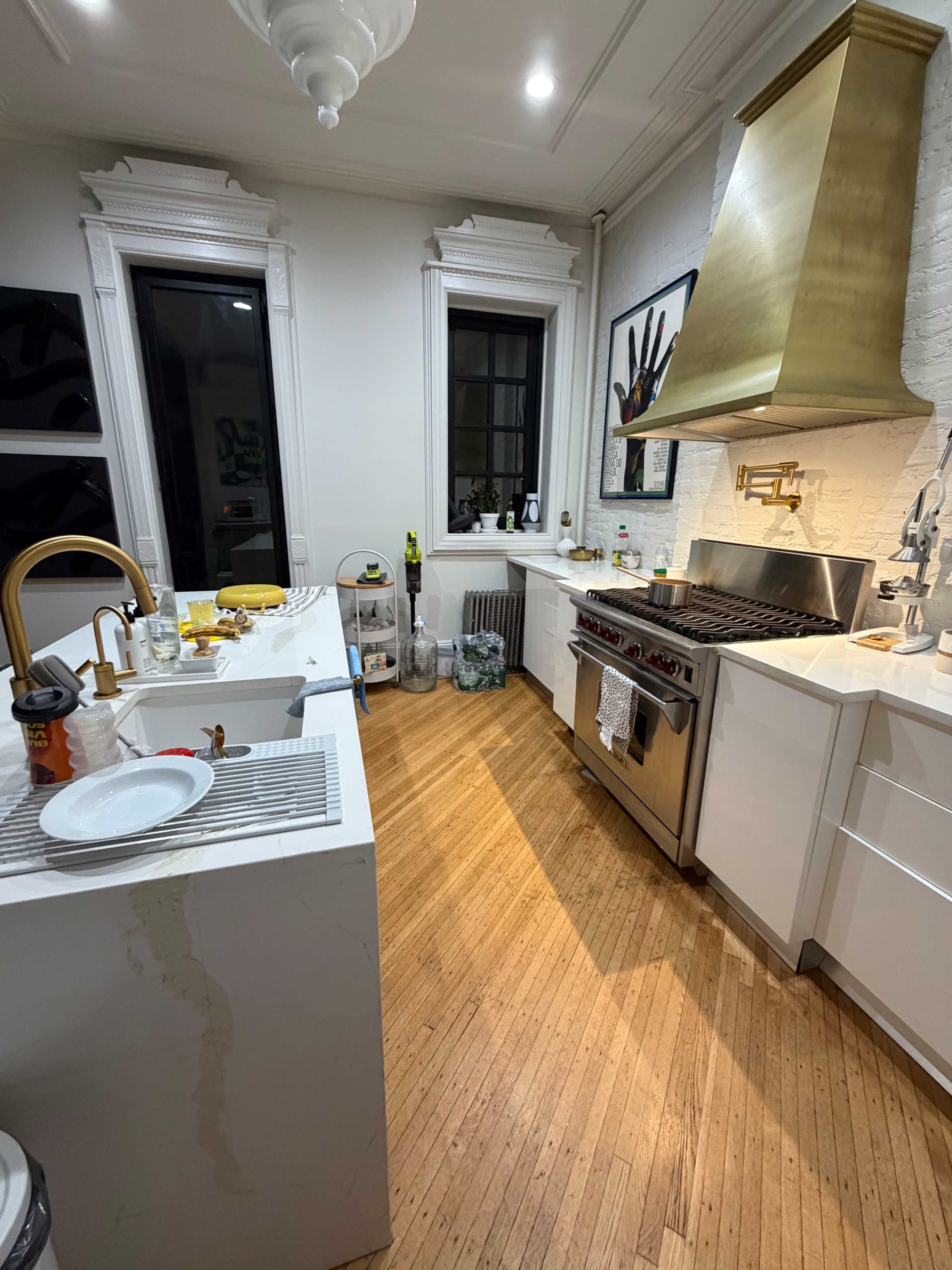 The kitchen features a gold range hood, white cabinetry, and wooden flooring, with a sink and countertop on one side.