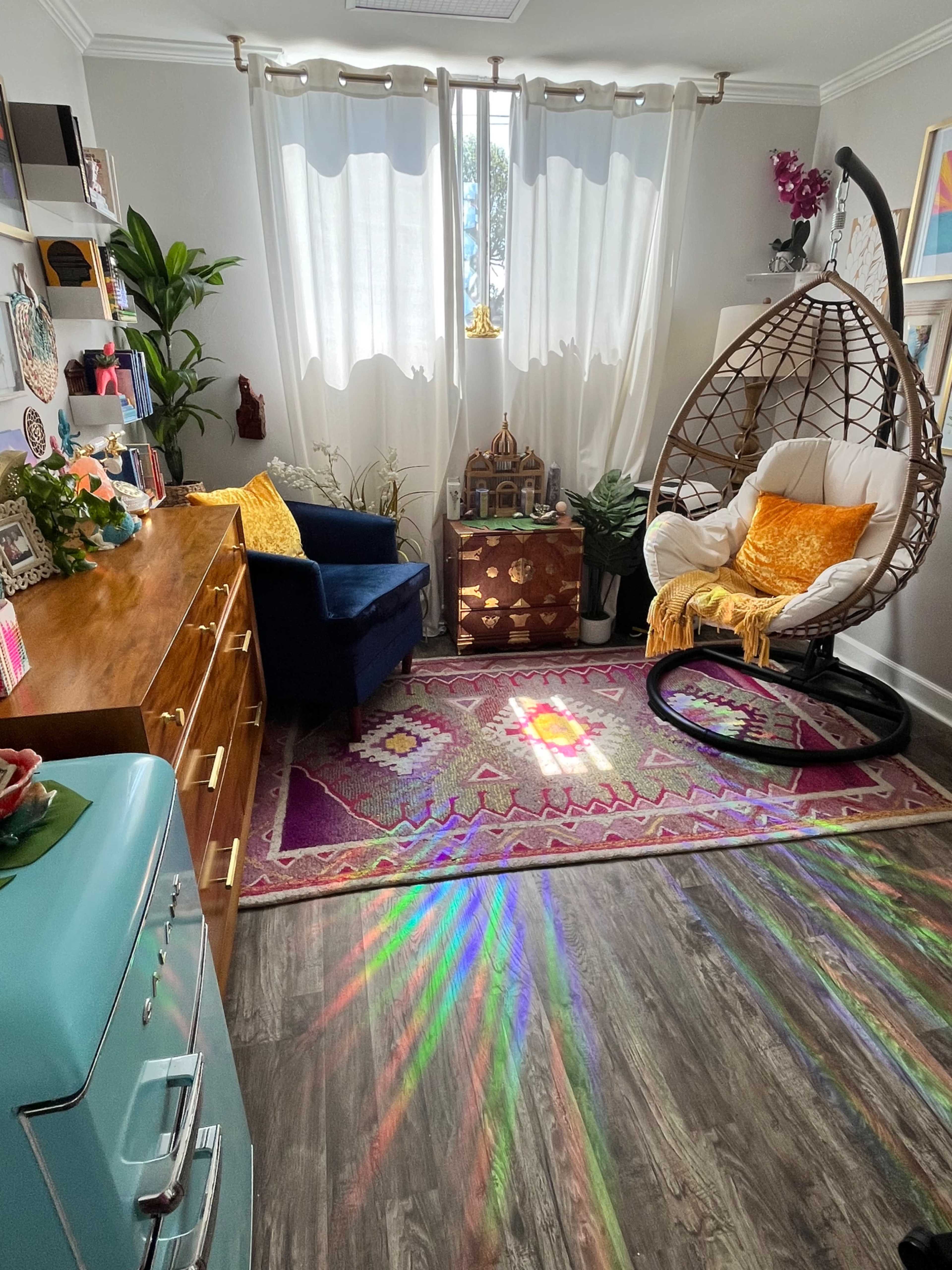 A cozy room features a hanging chair, a wooden dresser, and a colorful rug with sunlight casting rainbow patterns on the floor.