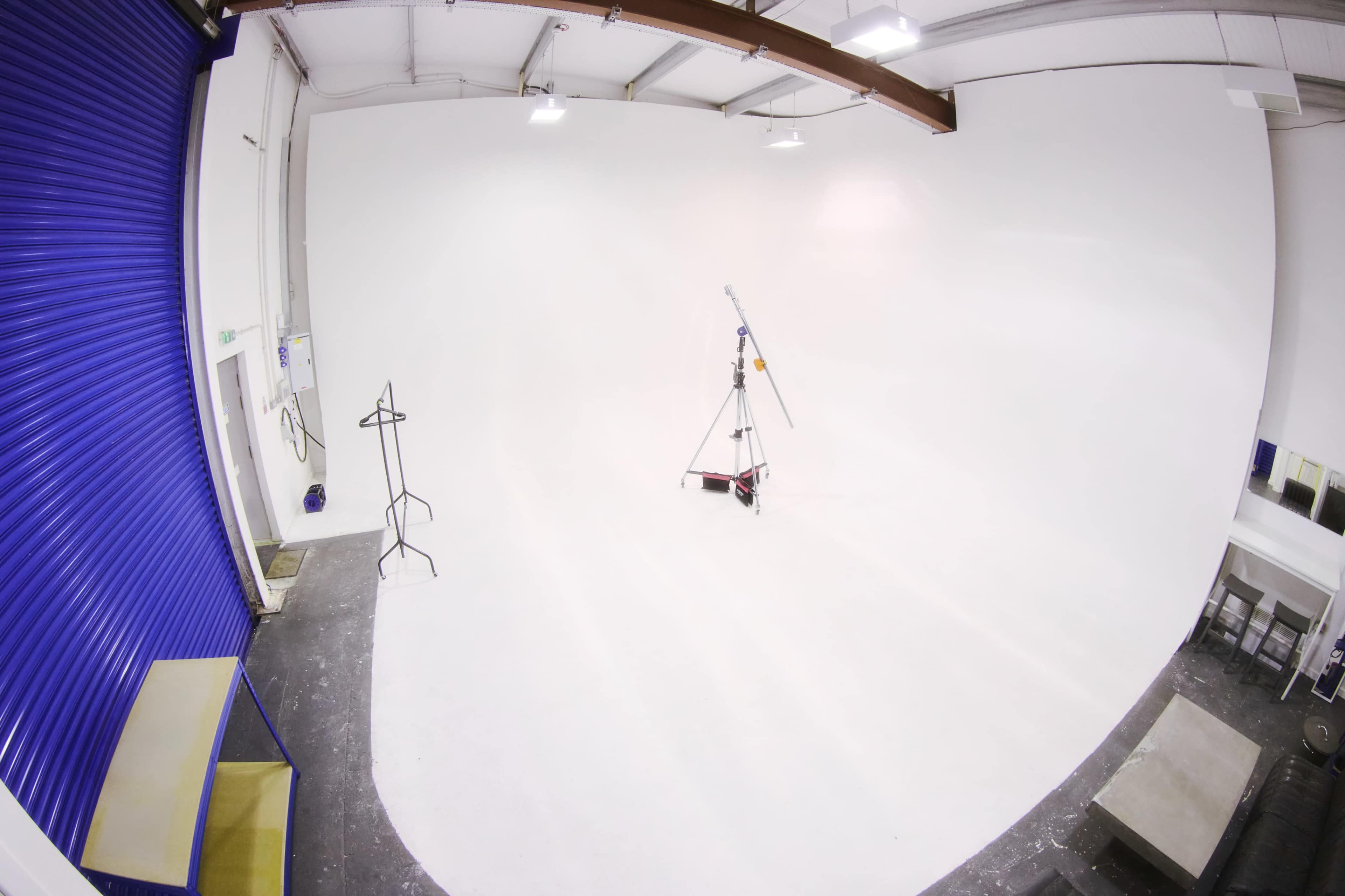 A spacious, white photography studio with a minimal setup, including a tripod and a clothing rack.