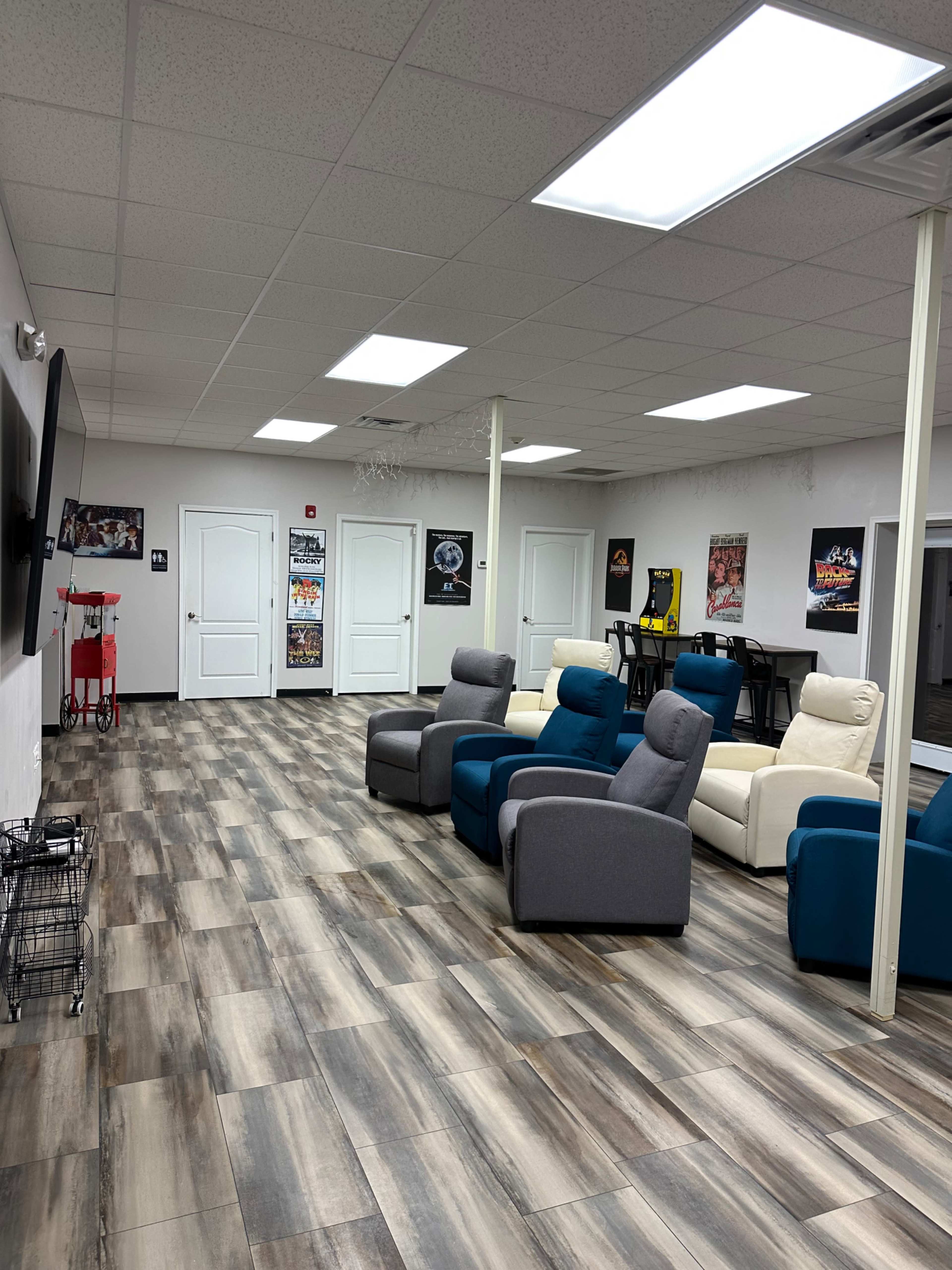 A spacious room with several recliner chairs, a TV mounted on the wall, and various posters displayed.