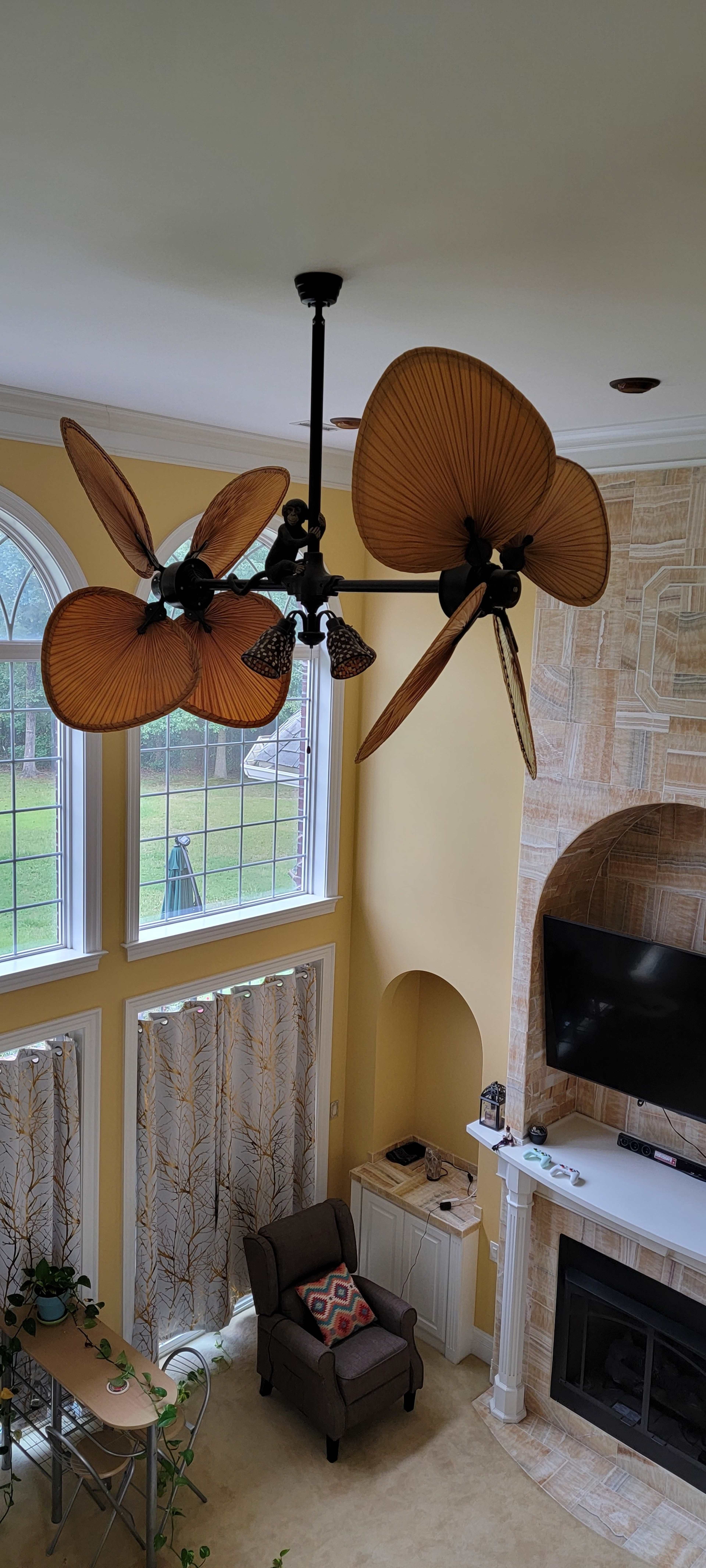 A spacious living room with a ceiling fan featuring large, decorative blades, and large windows that let in natural light.