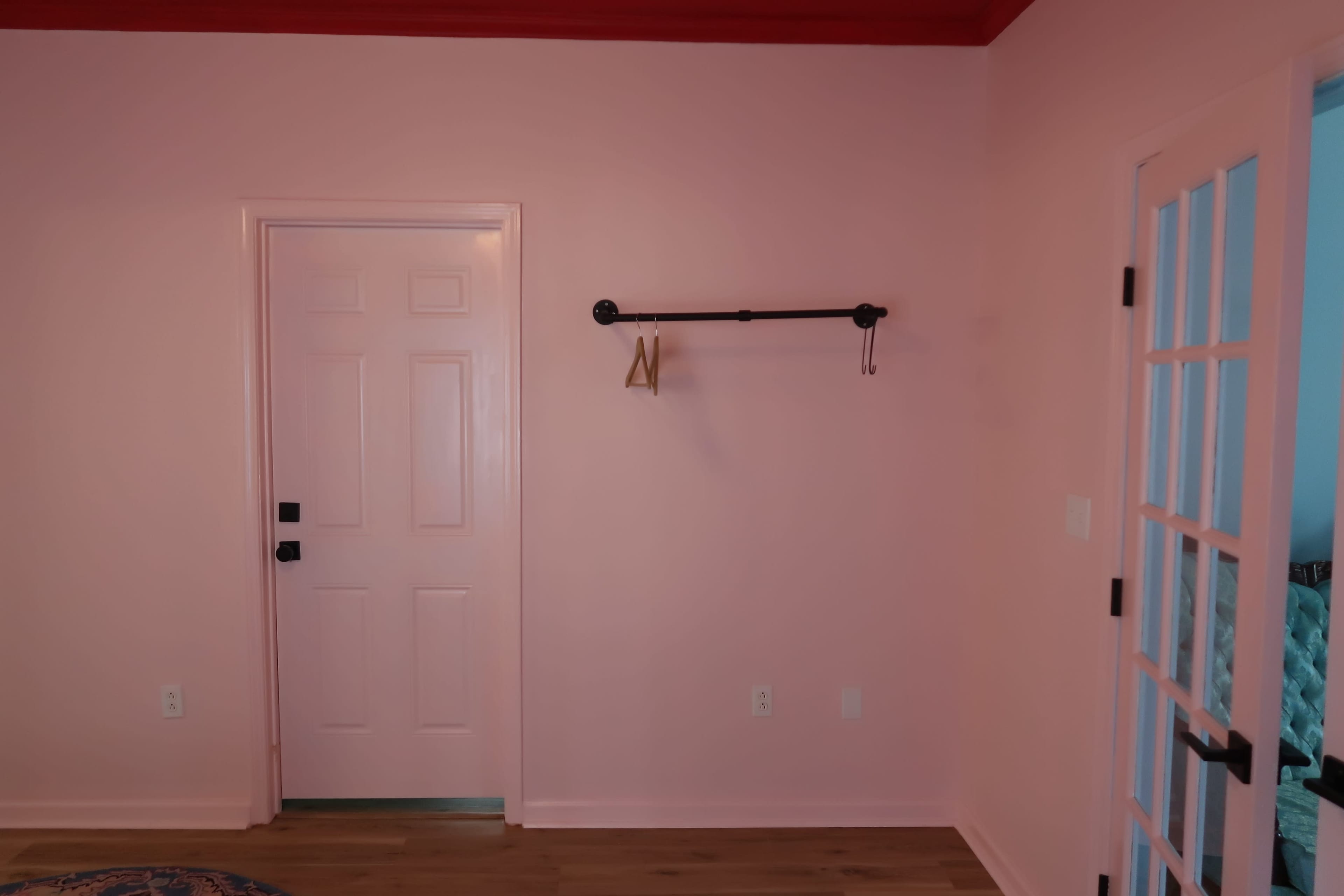 A pink-walled room with a white door and a black coat rack mounted on the wall.