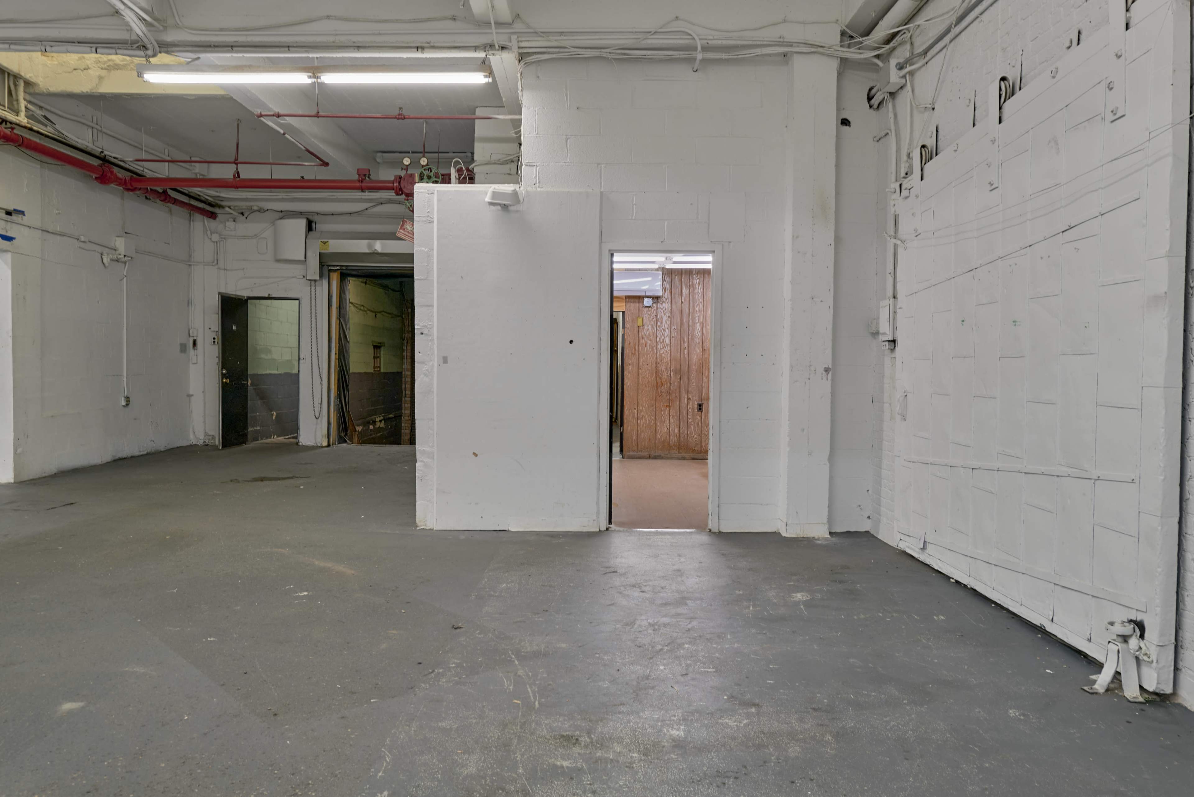 The image shows a vacant industrial space with gray concrete floors, white walls, and multiple doorways leading to different areas.