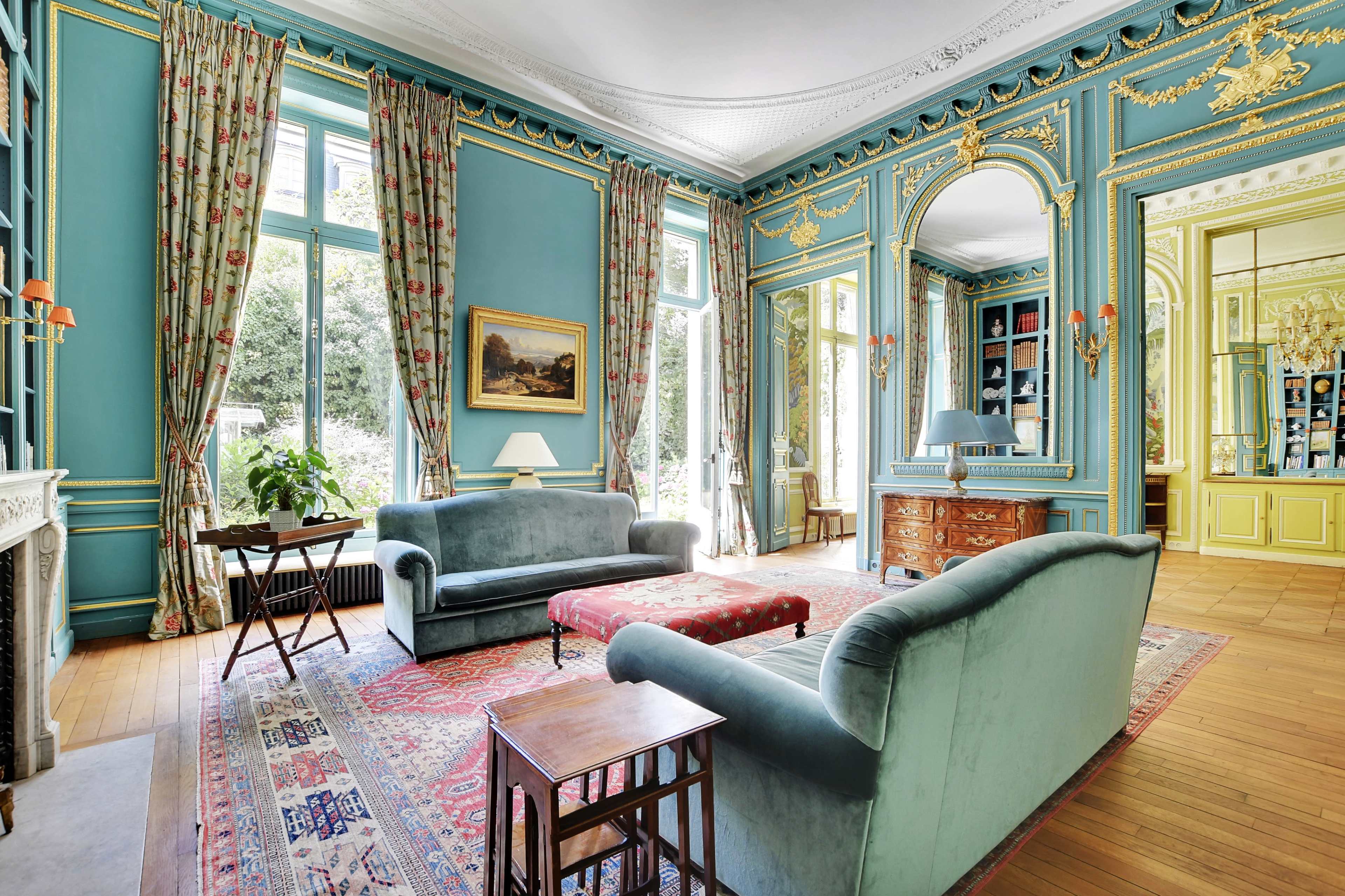 A bright, elegantly decorated living room with green walls, large windows, and classic furnishings including sofas, a coffee table, and a wooden cabinet.