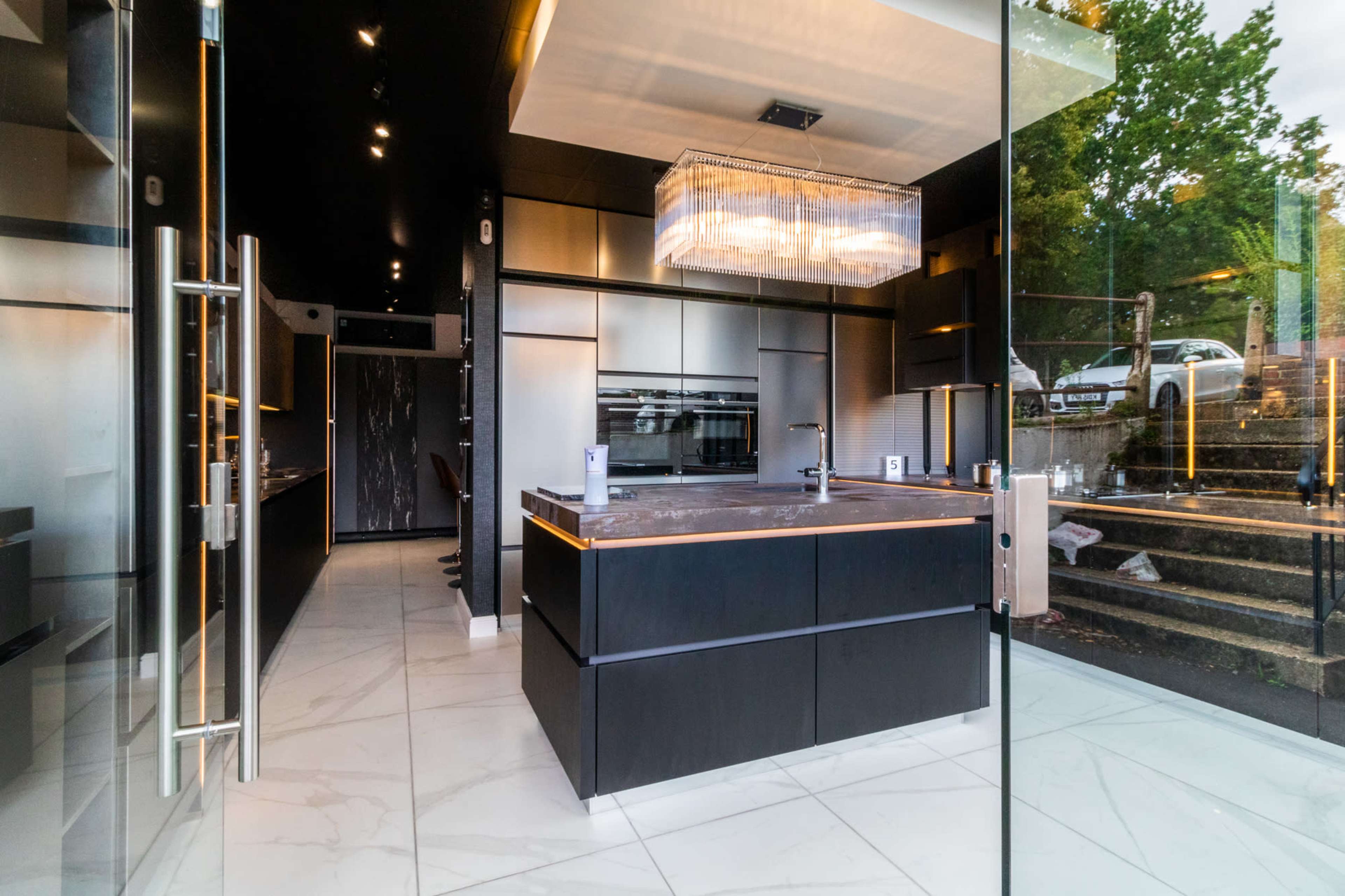 A modern kitchen with sleek black cabinetry, a large island with a marble countertop, and ample natural light from glass walls.