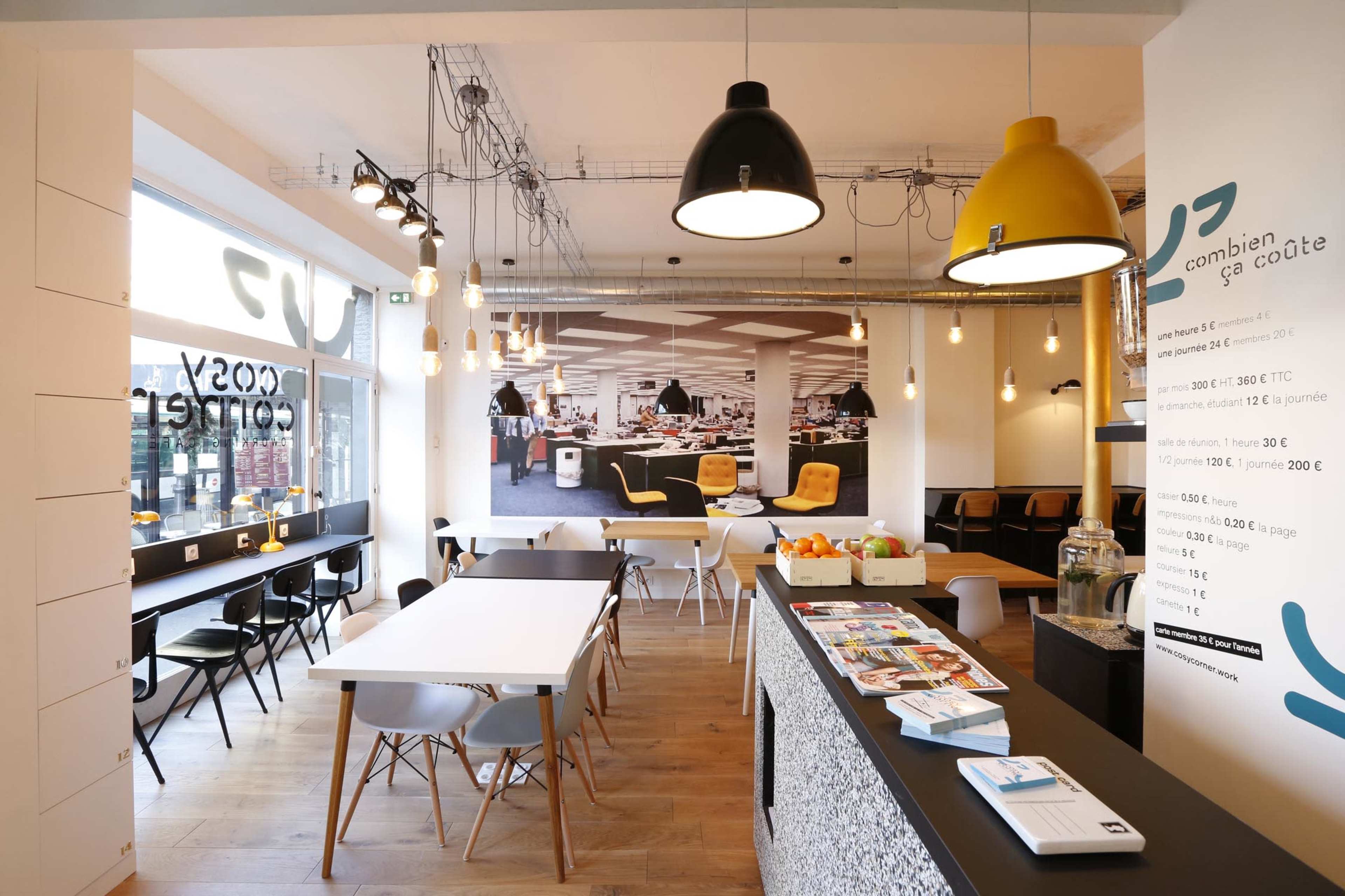 A modern café interior features a spacious seating area with a minimalist design, pendant lights, and a counter displaying informational brochures.