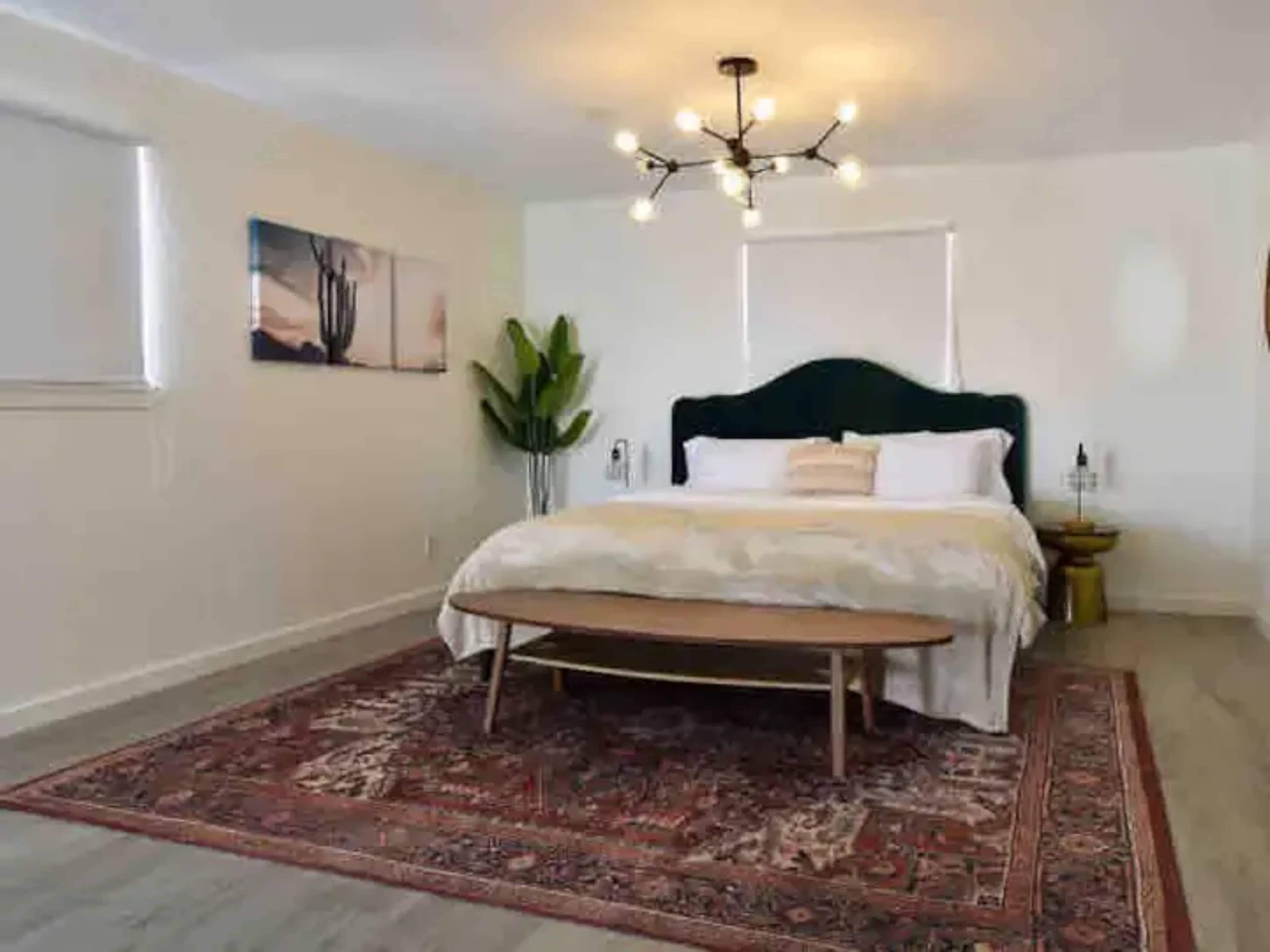 A modern, well-lit bedroom with a large bed, a wooden table in front, and decorative plants.