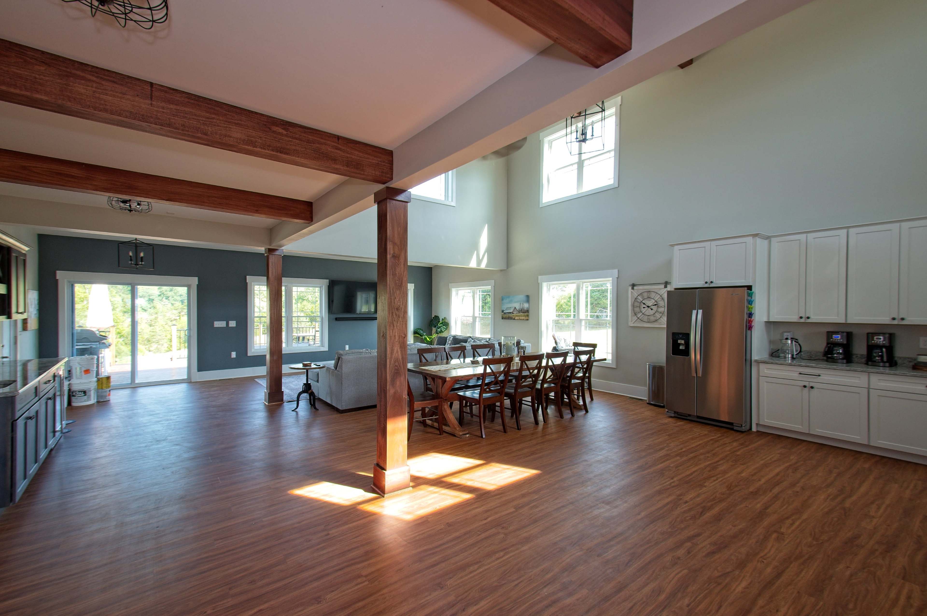 A spacious open-concept living area with wooden beams, large windows, a dining table, and a modern kitchen.