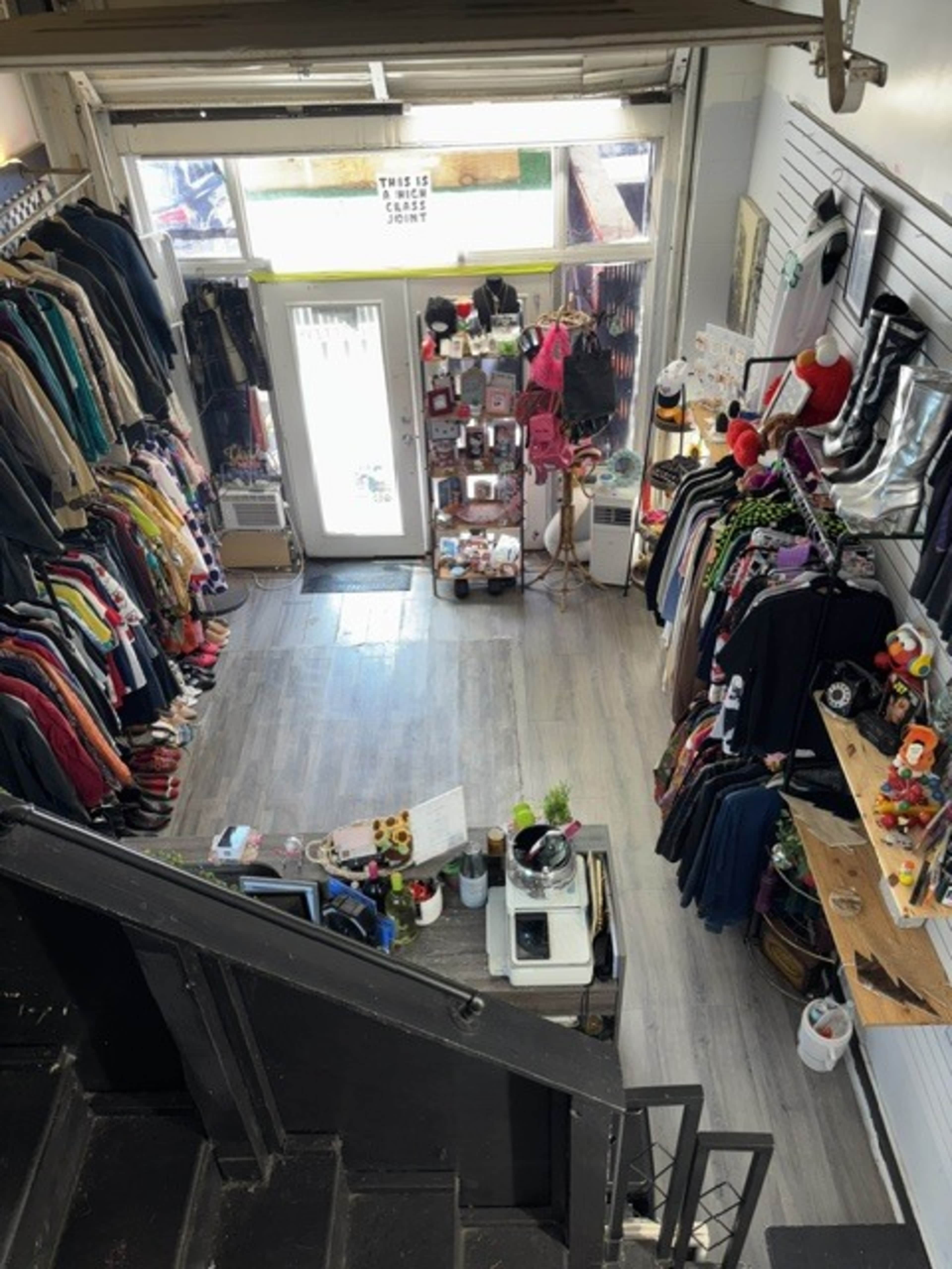 The image shows an overhead view of a retail shop filled with various clothing items on racks and shelves, a display of accessories, and a checkout counter.