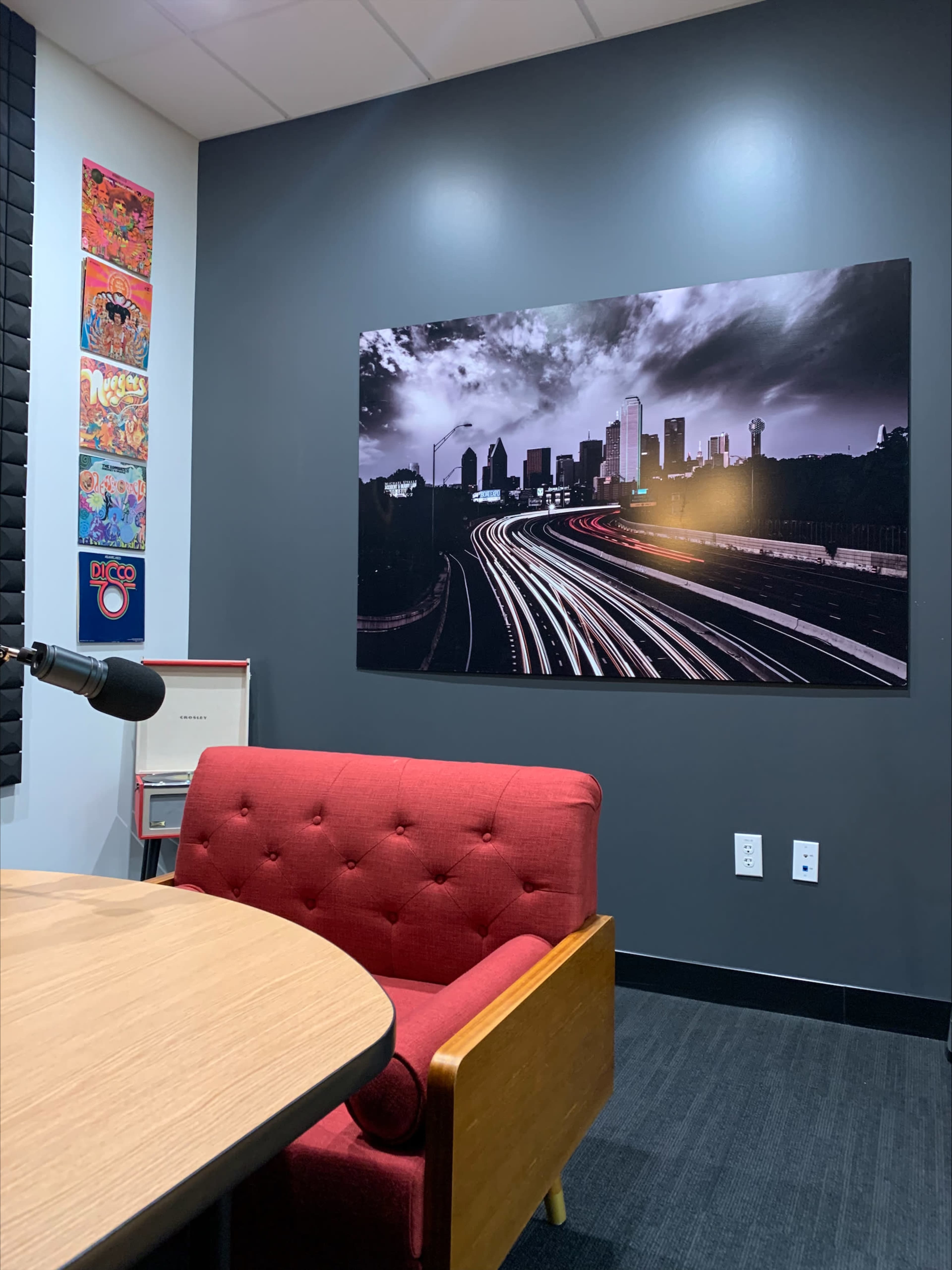 The image shows a cozy room with a red tufted chair, a microphone, and a large black-and-white photograph of a cityscape on the wall.