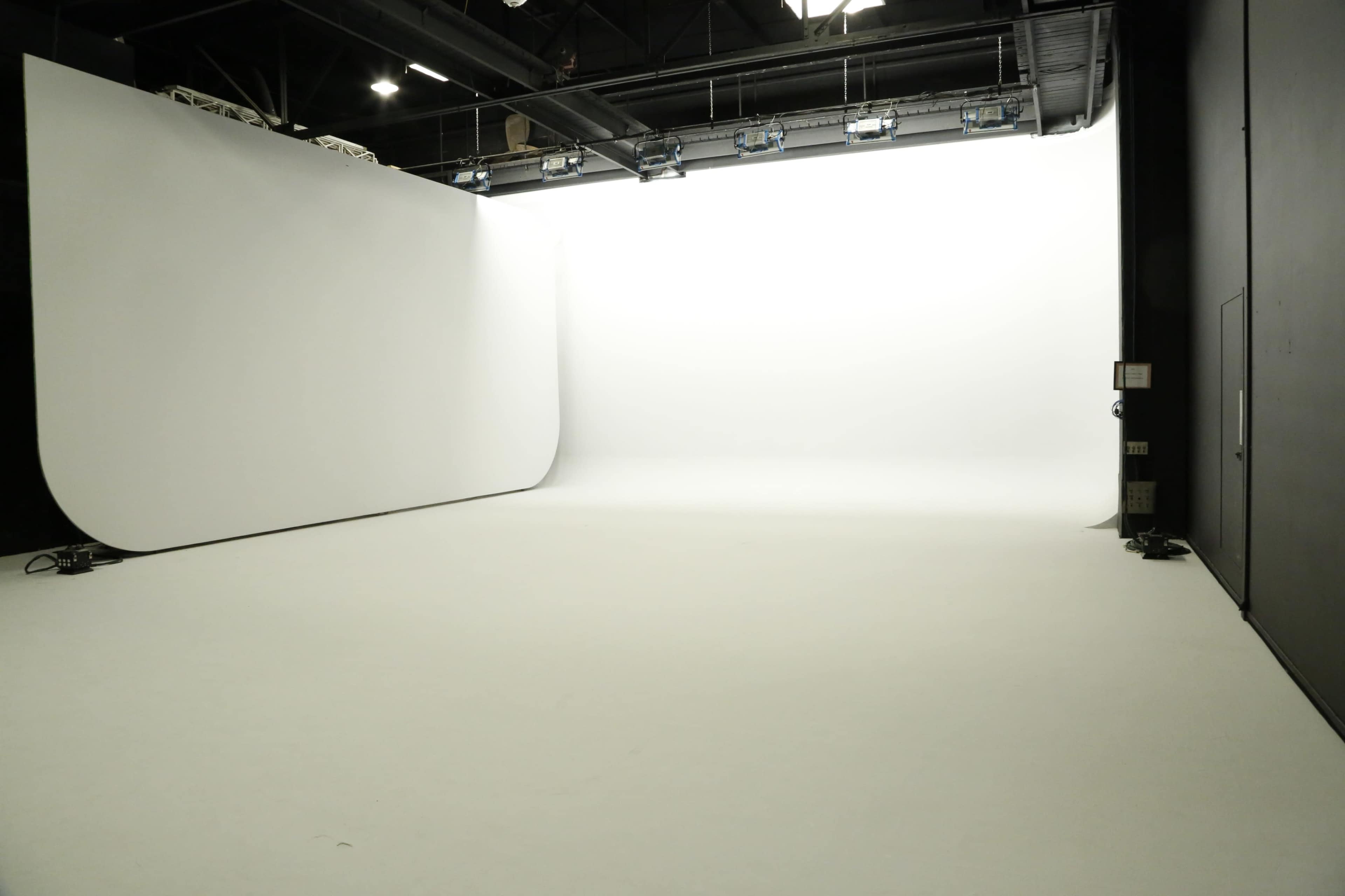 A large, empty photography studio with a seamless white backdrop and a smooth white floor.