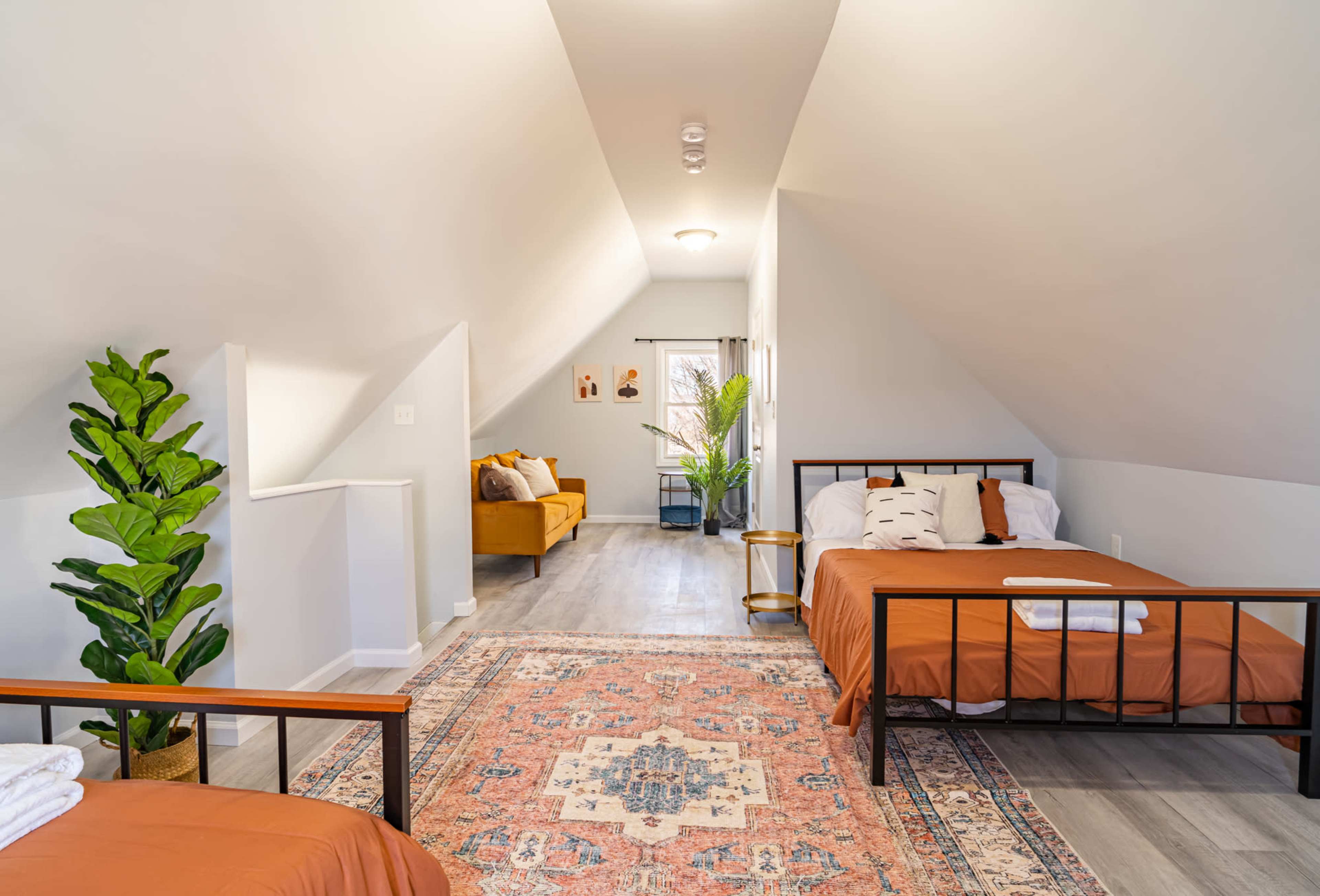 The room features two beds, a small seating area with a couch, and a decorative plant, all set beneath a sloped ceiling.