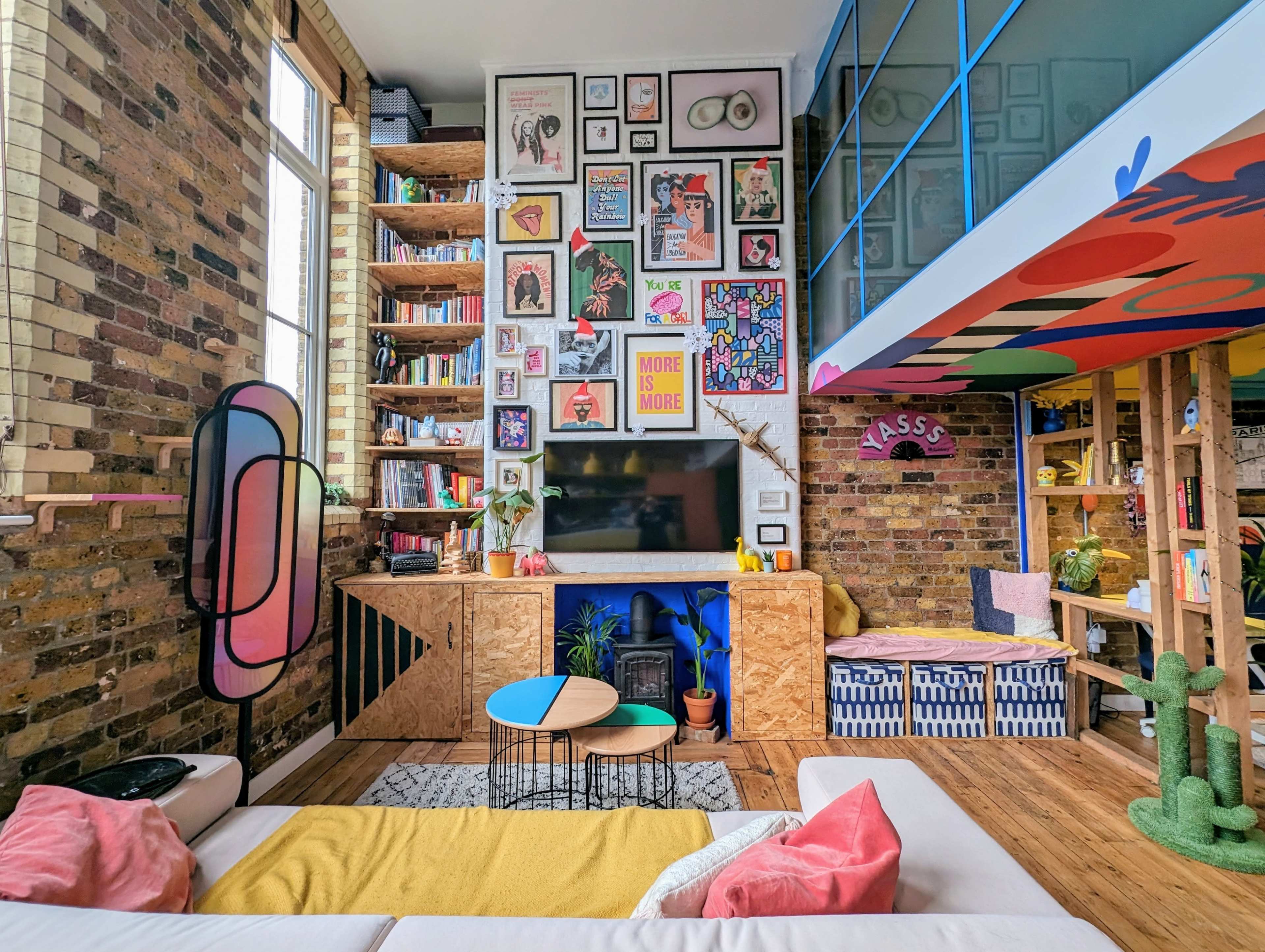 A stylish living room featuring a mix of colorful art on the walls, a wooden bookshelf filled with books, and a variety of modern furniture.
