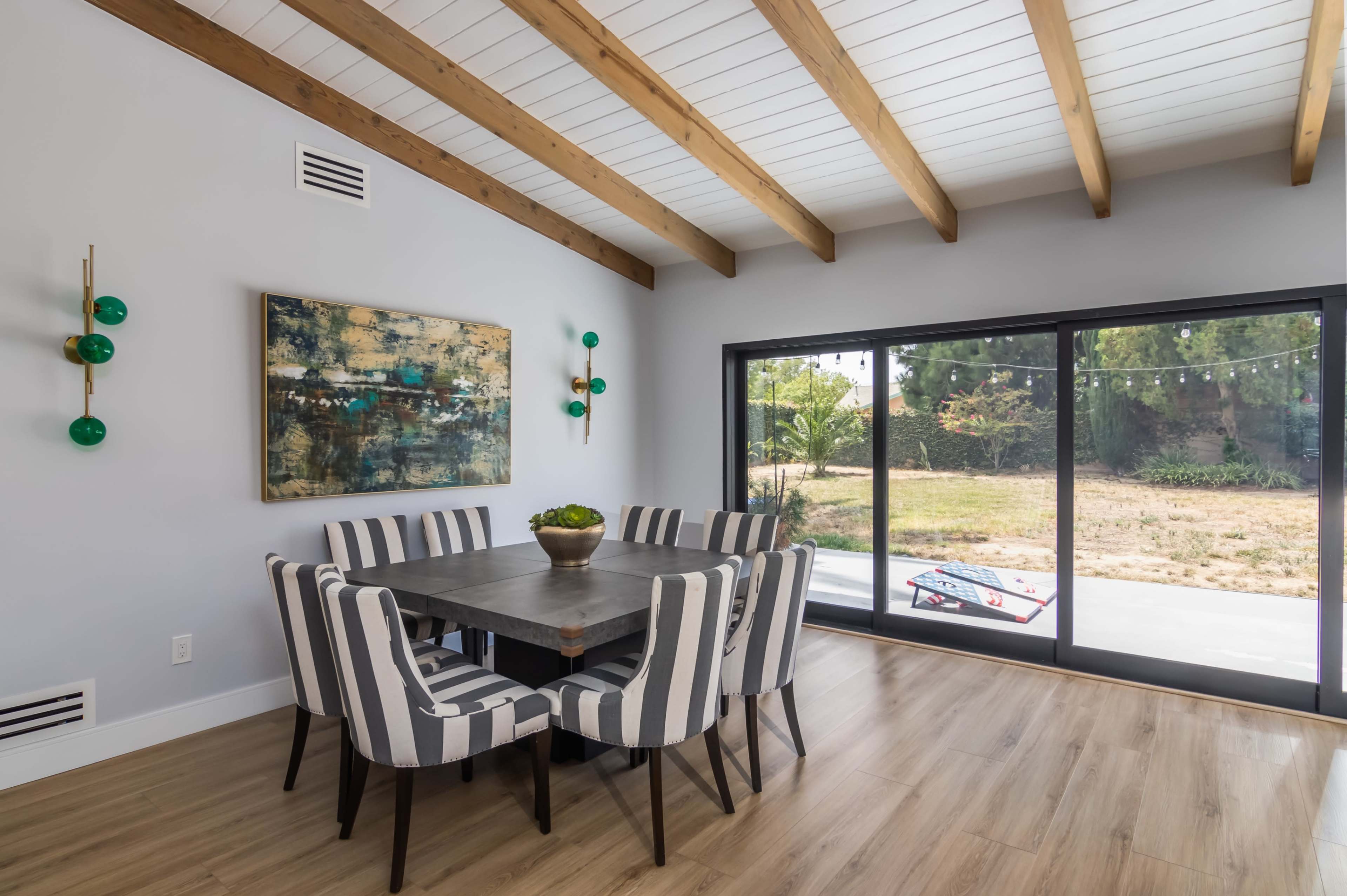 A modern dining area features a rectangular table surrounded by striped chairs, with a large window overlooking an outdoor space.