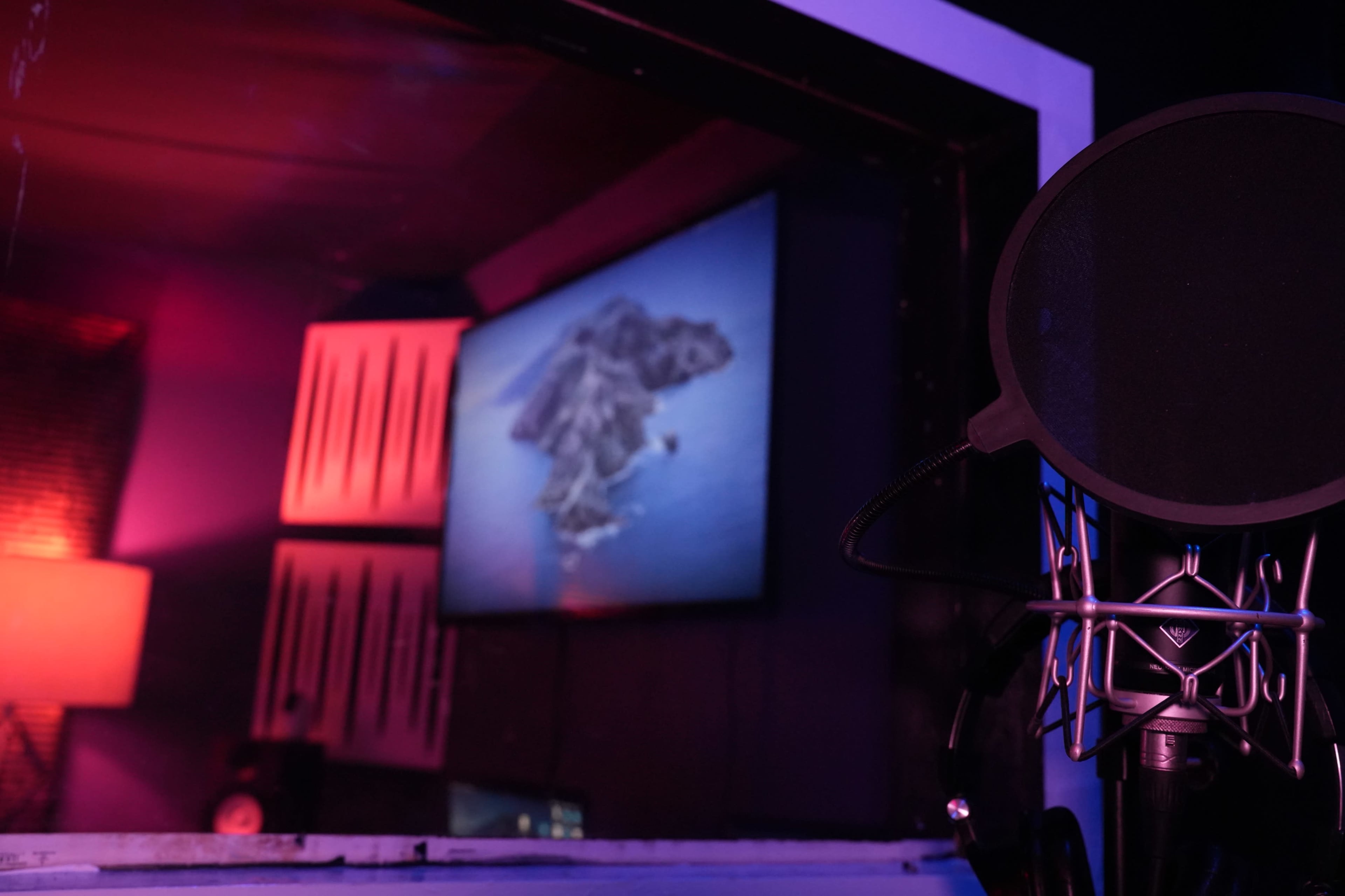 A microphone stands in the foreground of a recording studio, with a screen displaying an island image in the background.