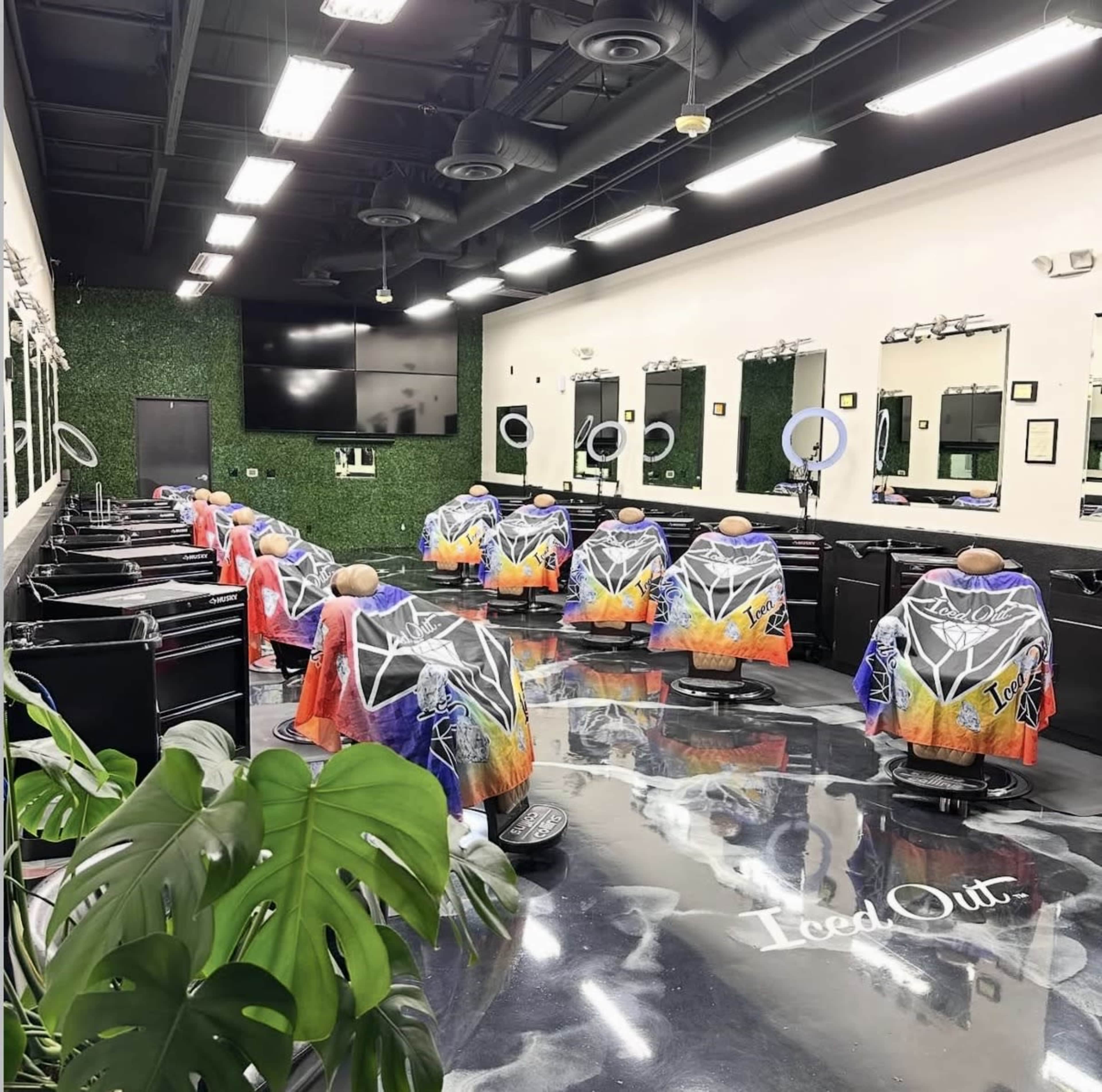 The image shows the interior of a barber shop with several black salon chairs, each covered with vibrant capes, arranged in rows against green wall decor.