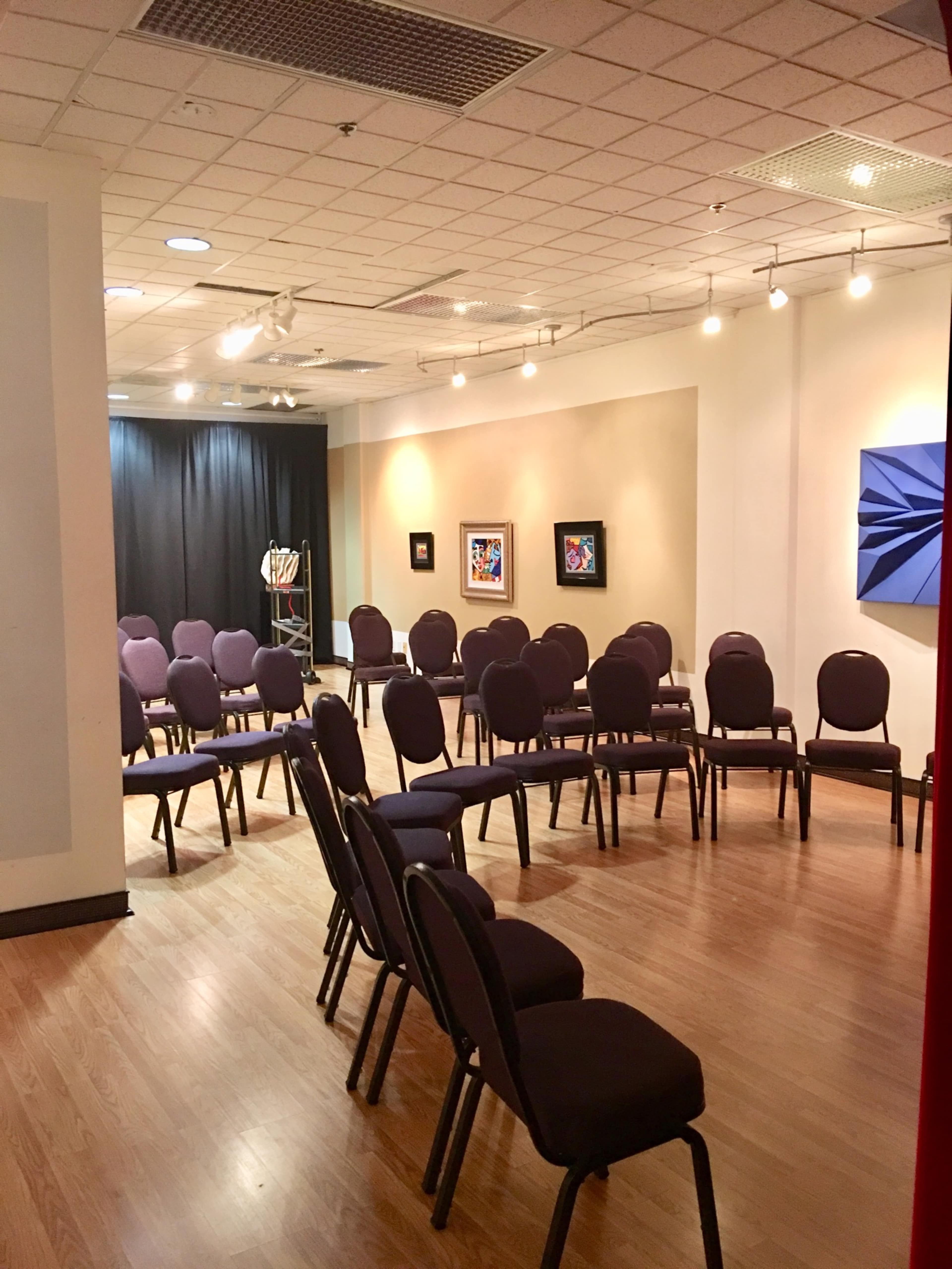 A room with several rows of purple chairs arranged facing a black curtain, with artwork displayed on the walls.