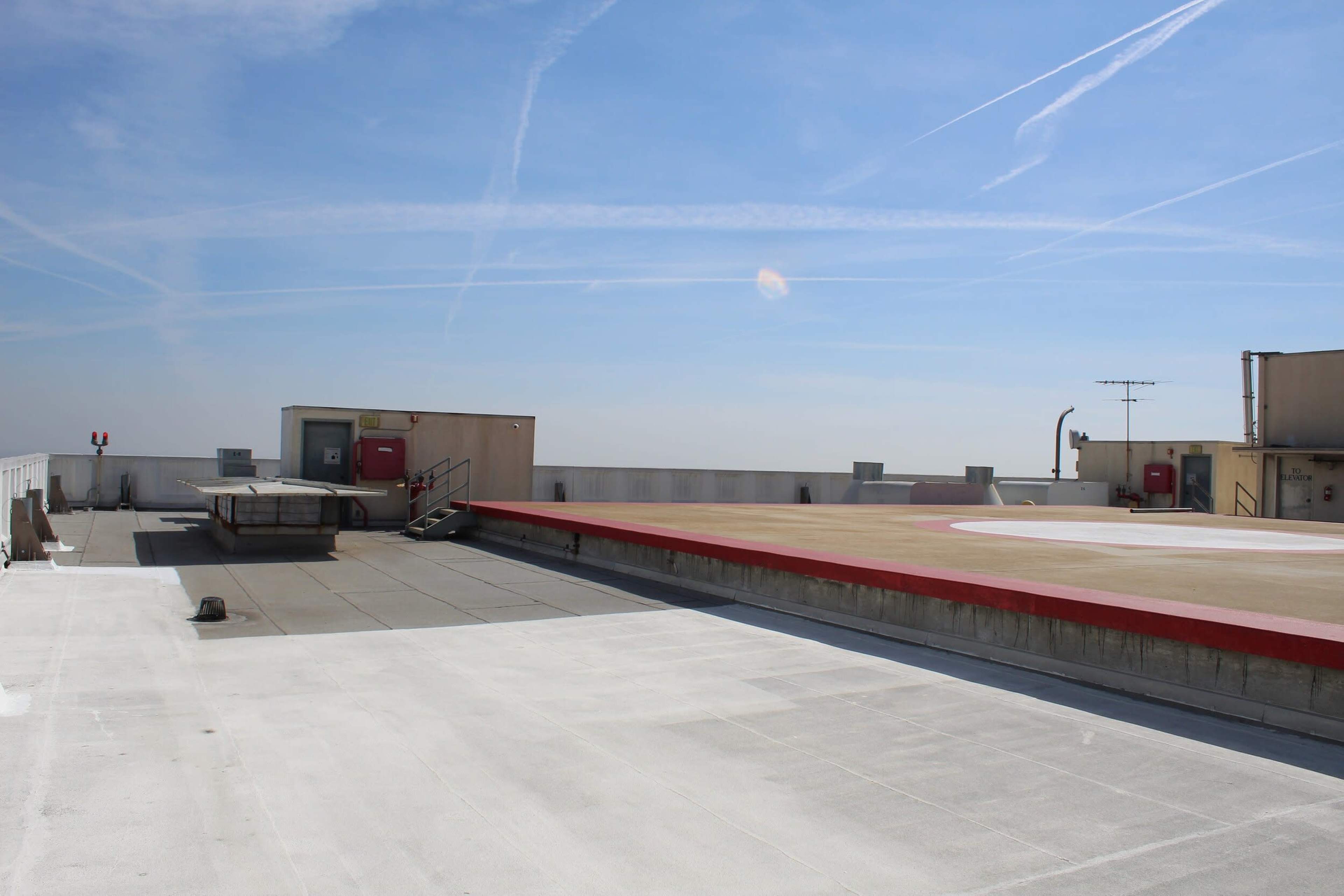 A flat rooftop features a helipad marked with a red perimeter, along with several utility structures and a clear blue sky overhead.
