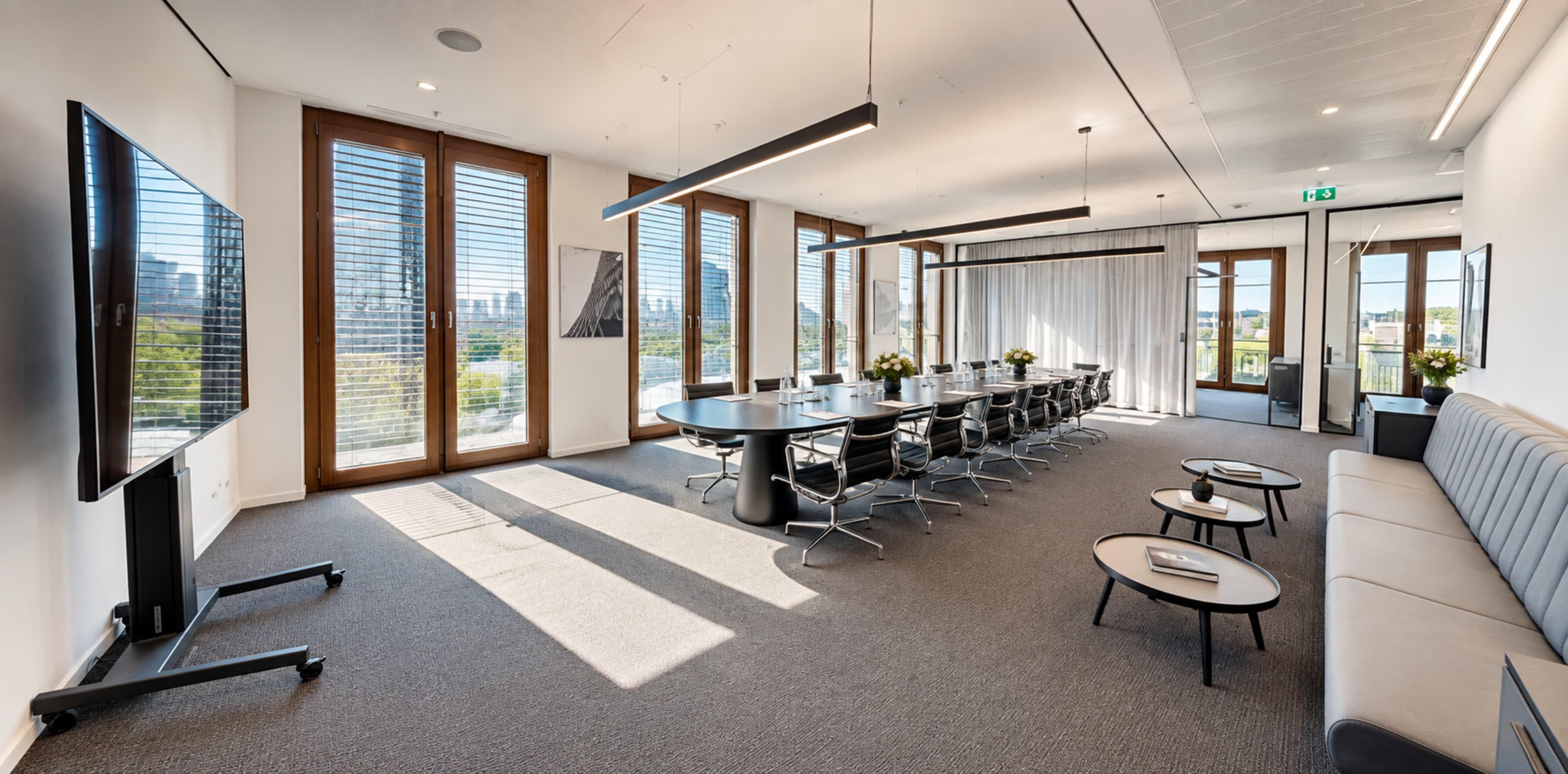 A modern conference room features a long table with seating for fourteen, large windows providing natural light, and a sleek, minimalistic design.