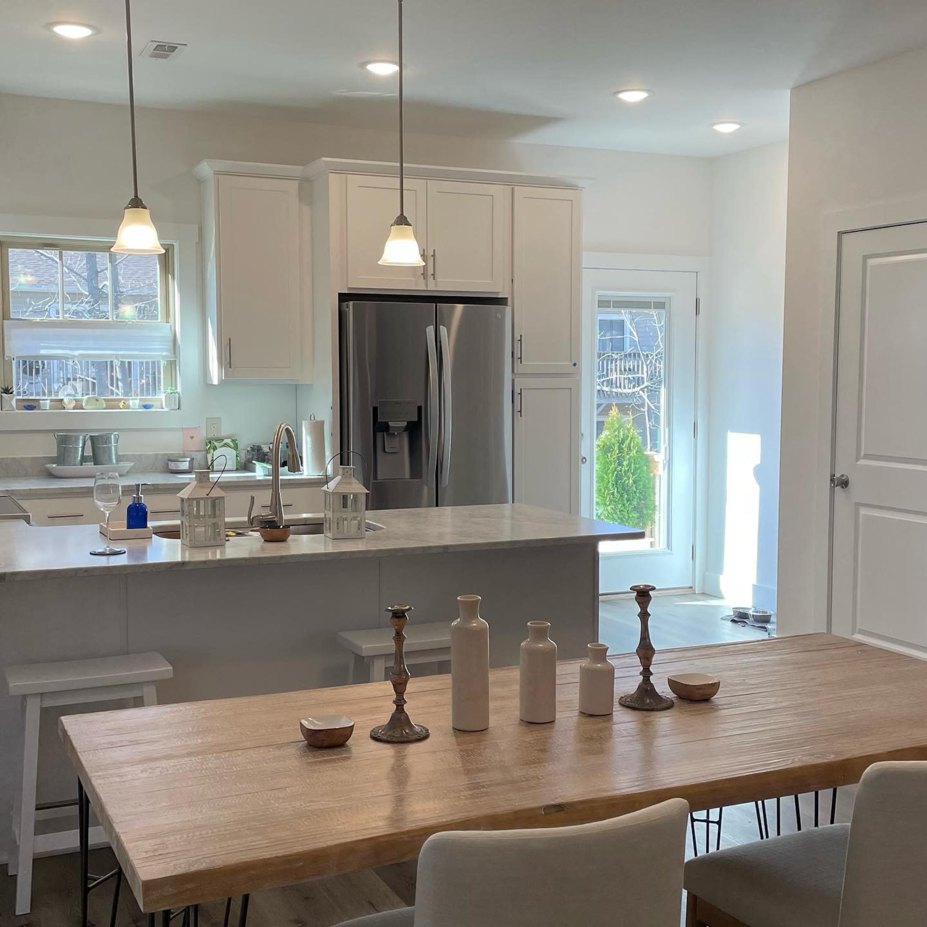 A modern kitchen features a central island with gray countertops, white cabinetry, and a dining table set with various decorative vases and candleholders.