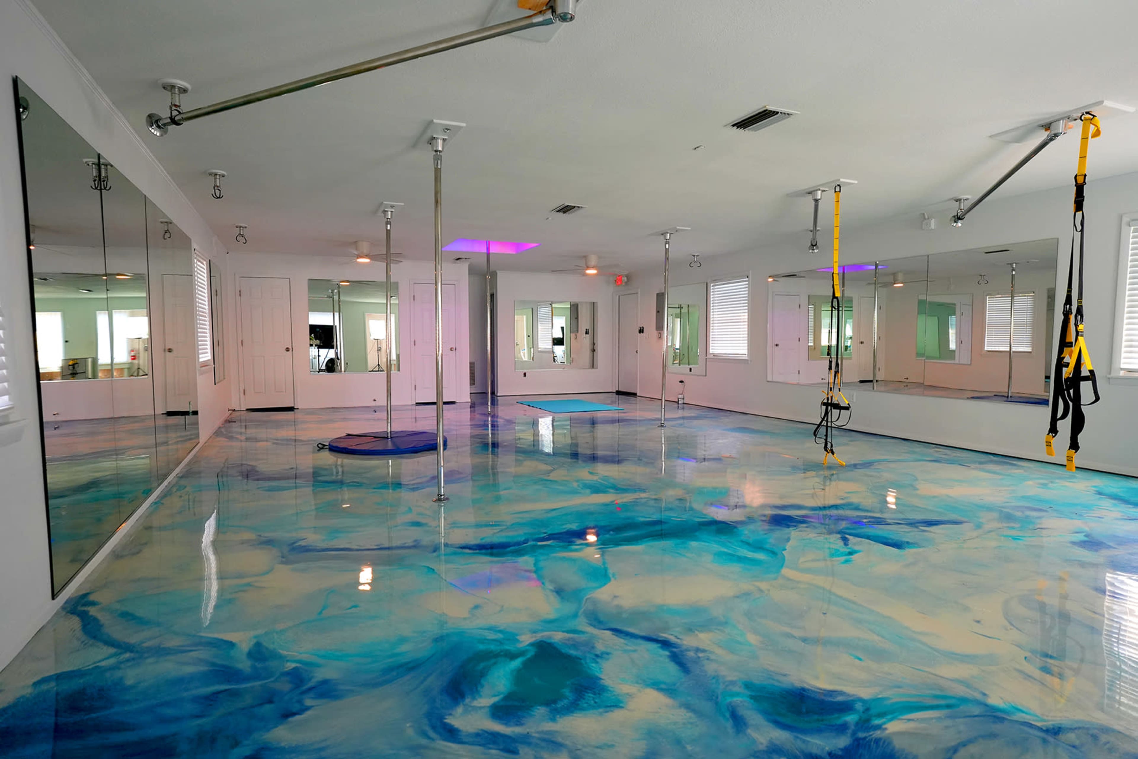 A spacious room with a glossy, blue-and-white marbled floor, equipped with mirrors and suspension training equipment hanging from the ceiling.
