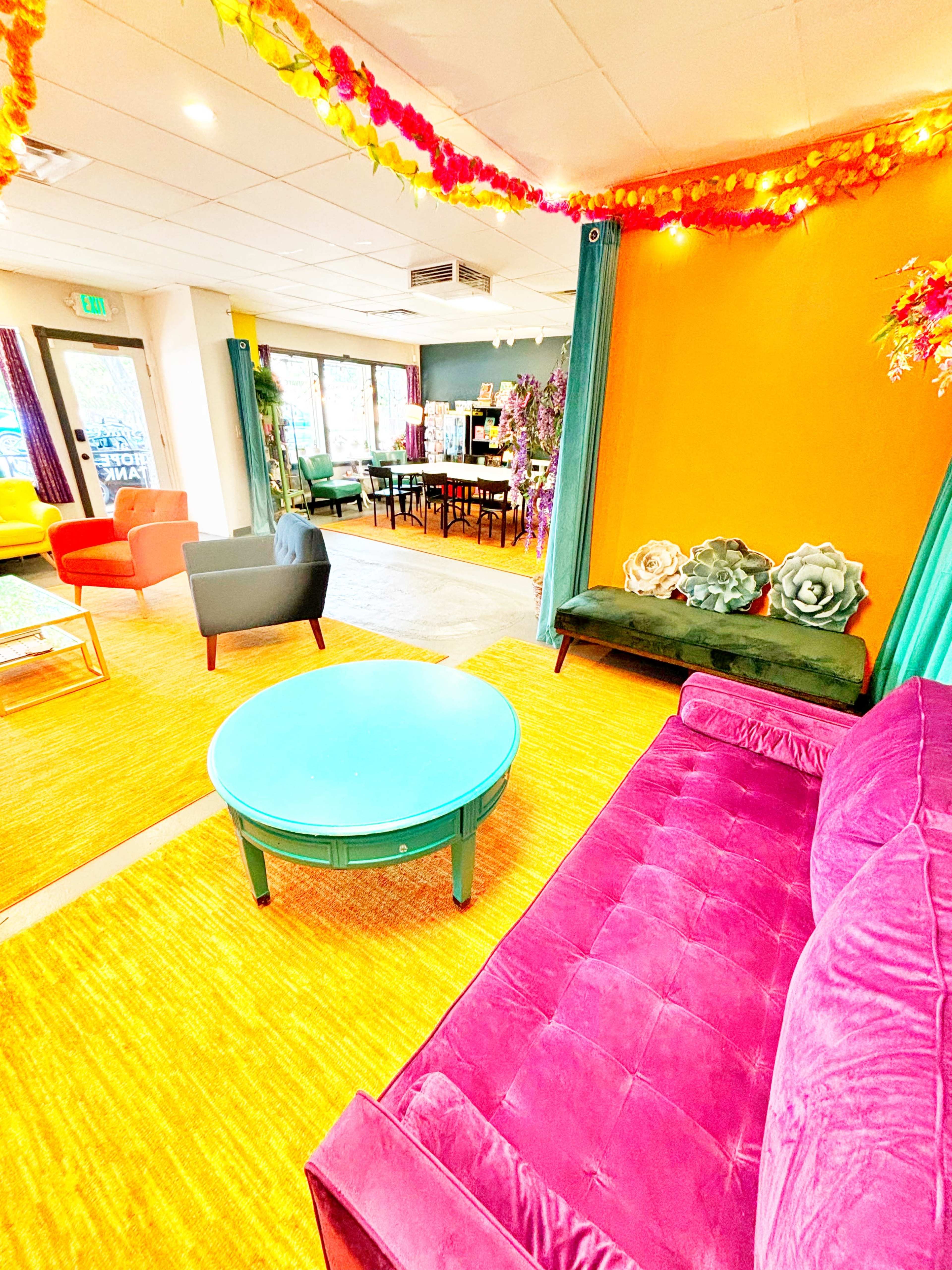 A vibrant interior space featuring colorful seating, a round turquoise coffee table, and decorative floral elements on the walls.