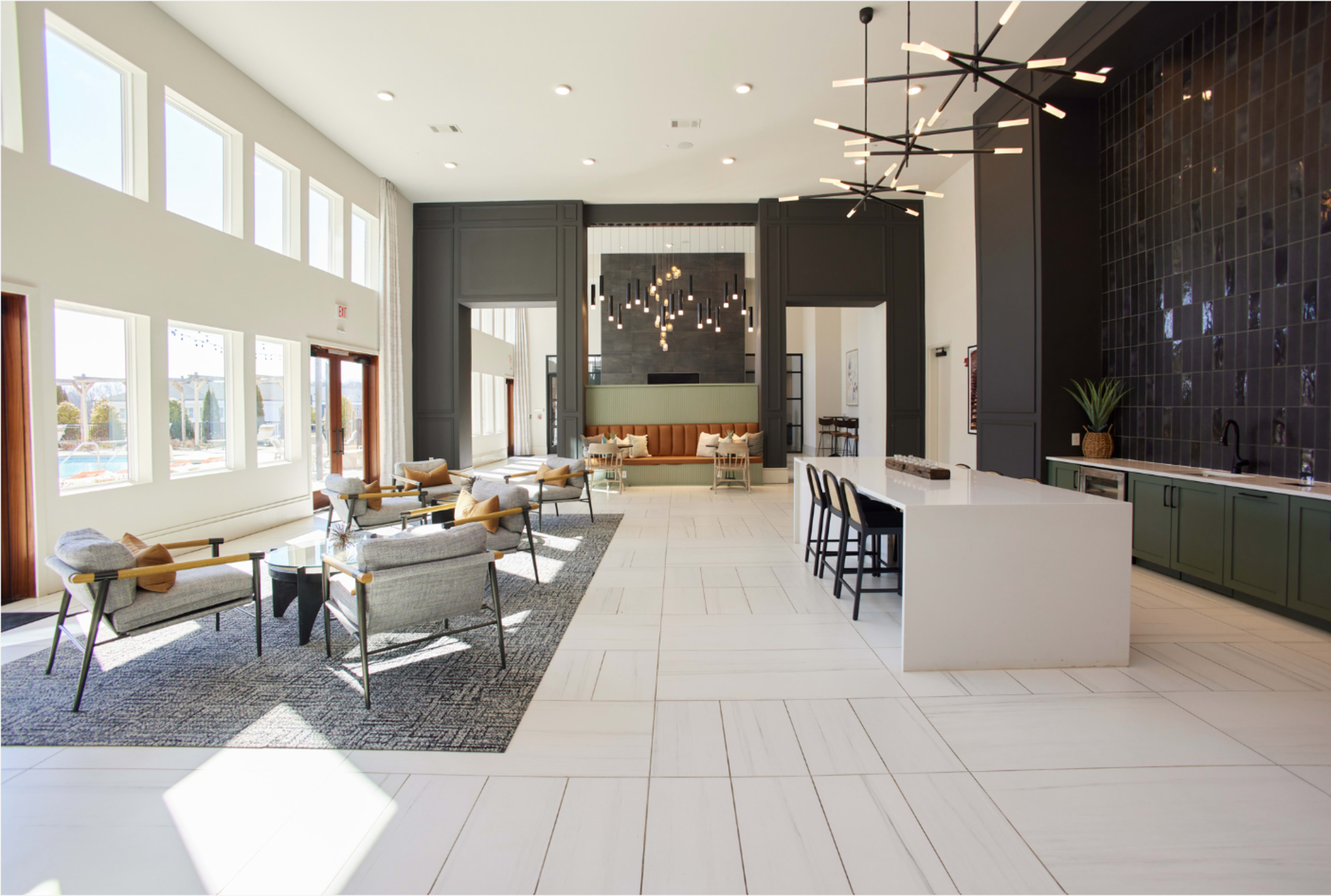 The image shows a spacious and modern lounge area featuring comfortable seating, large windows, and a sleek kitchen bar.