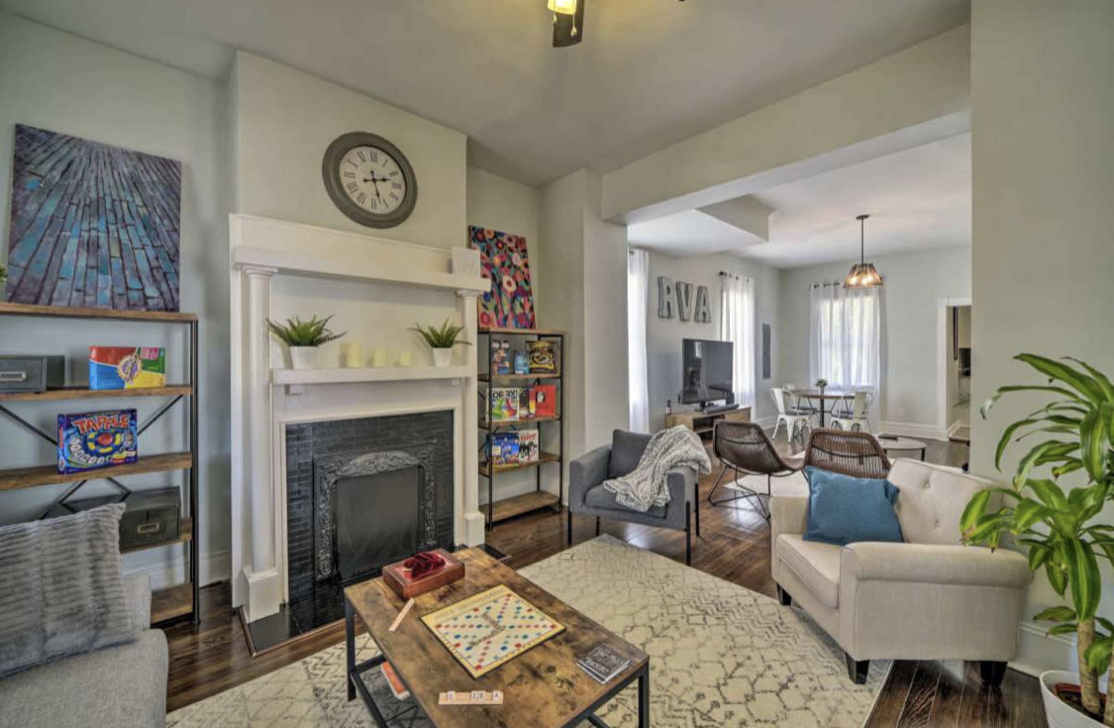 A cozy living room with a fireplace, a large area rug, and various seating options, leading into a dining area with a table and chairs.