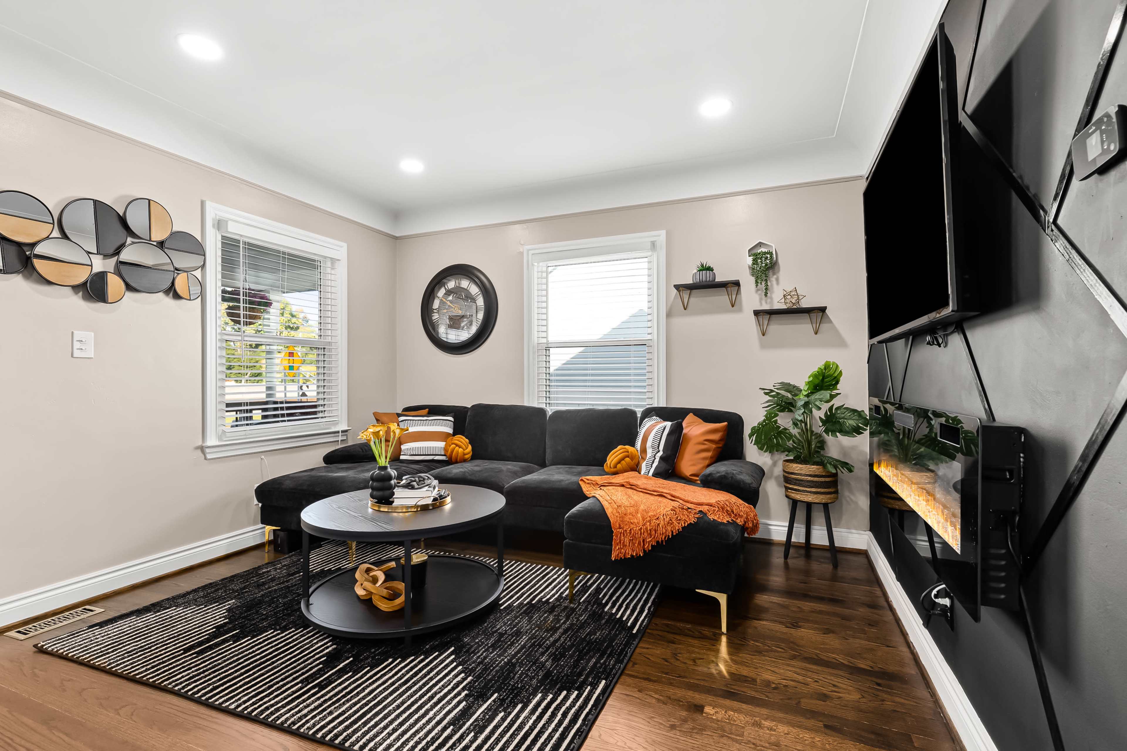 A modern living room features a dark sectional sofa, a round coffee table, and a wall-mounted television, with decorative items and plants enhancing the space.