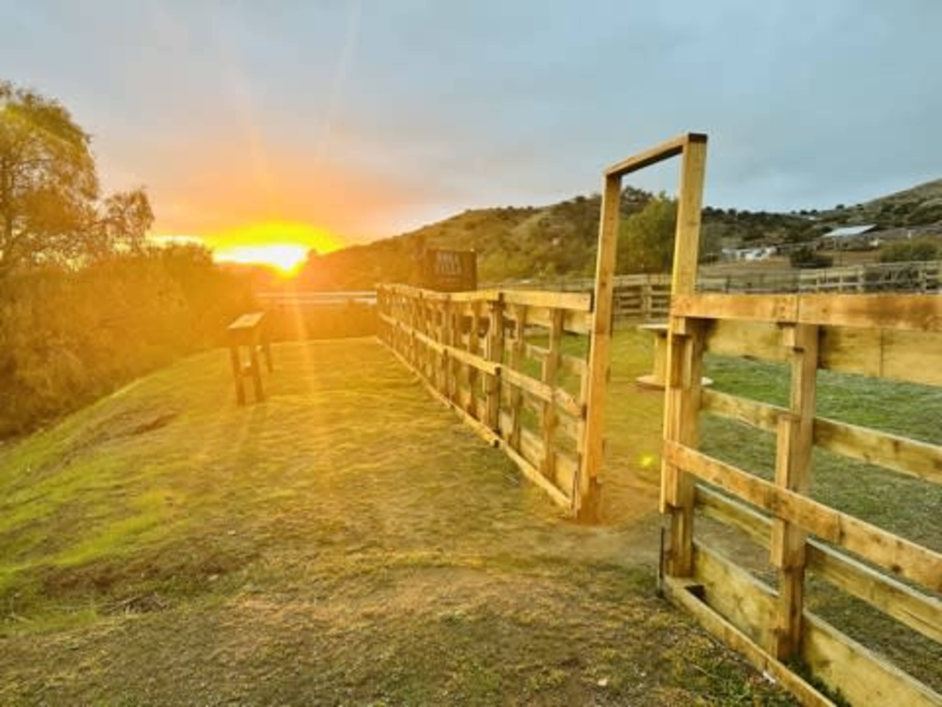 The image shows a wooden corral with a sunset in the background, casting warm light over the landscape.