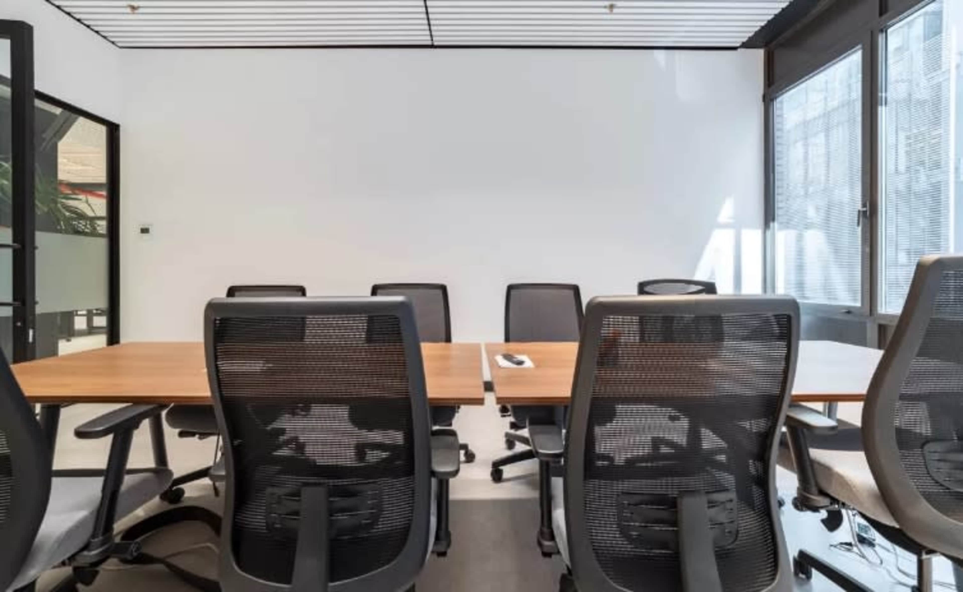 A modern conference room features a large wooden table surrounded by several ergonomic office chairs.