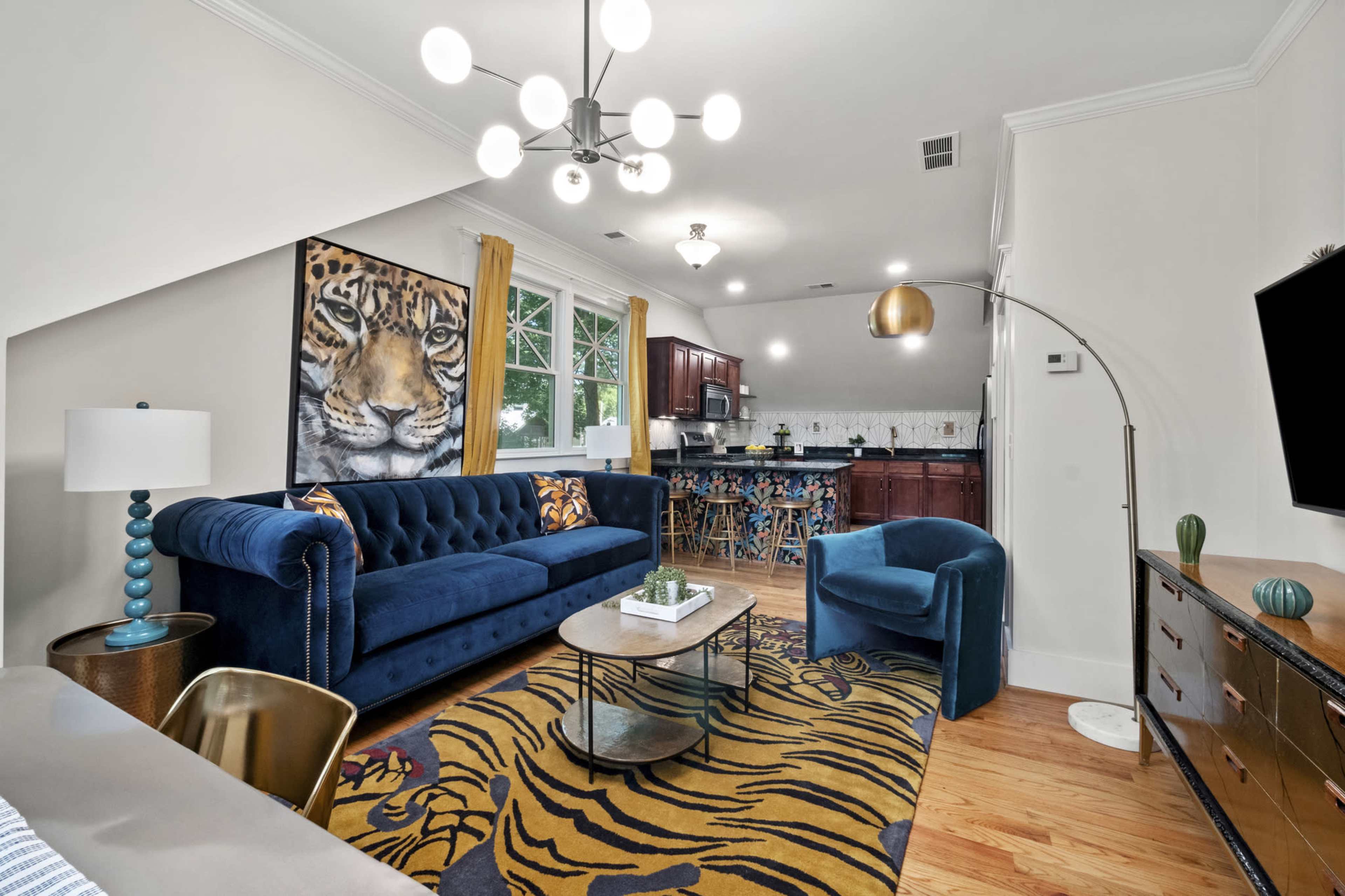 The scene features a living room with a blue sofa, a round coffee table, and a large wall art of a tiger, leading into a kitchen area in the background.
